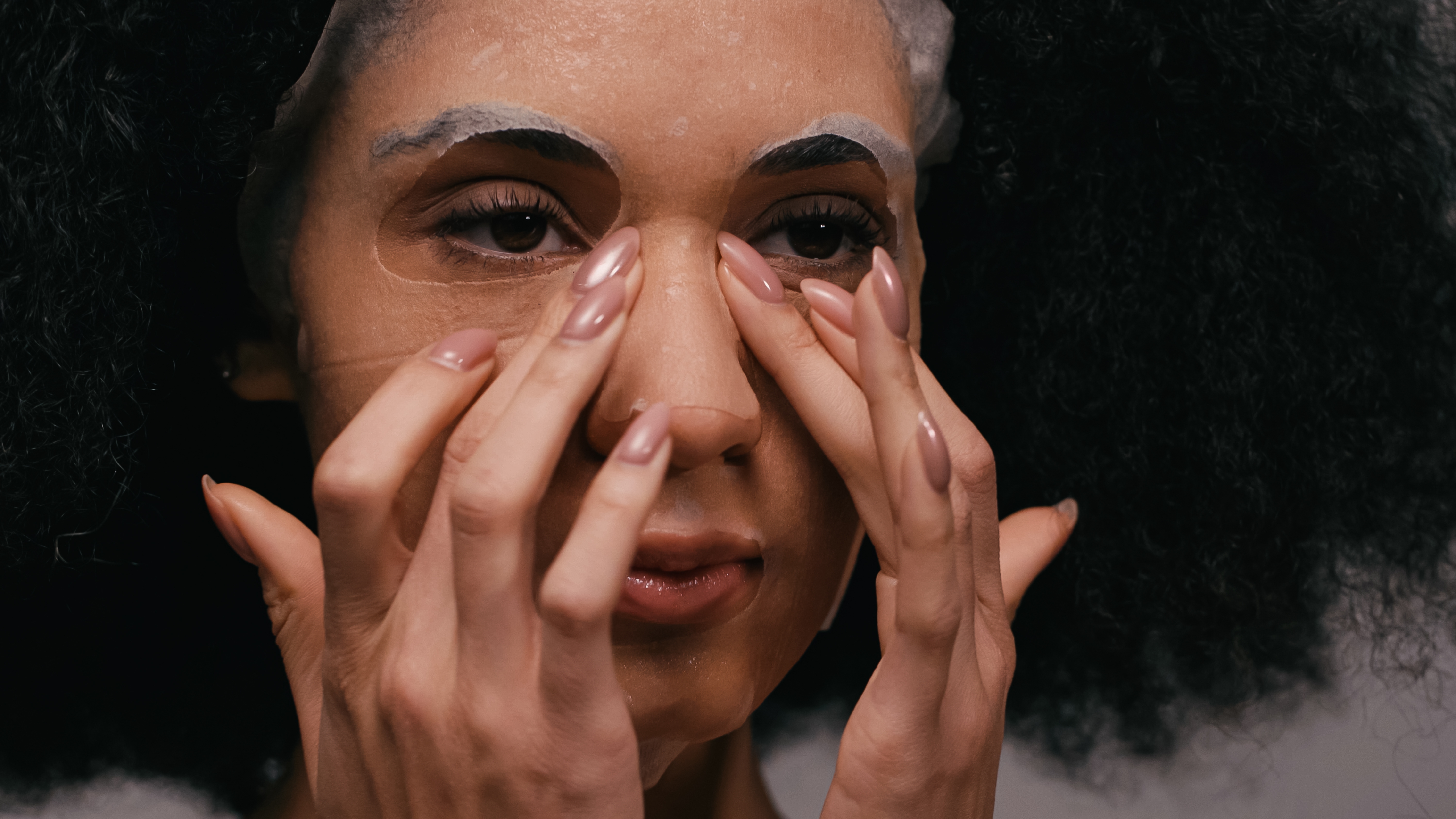 A woman placing a sheet mask on her face. | Source: Shutterstock