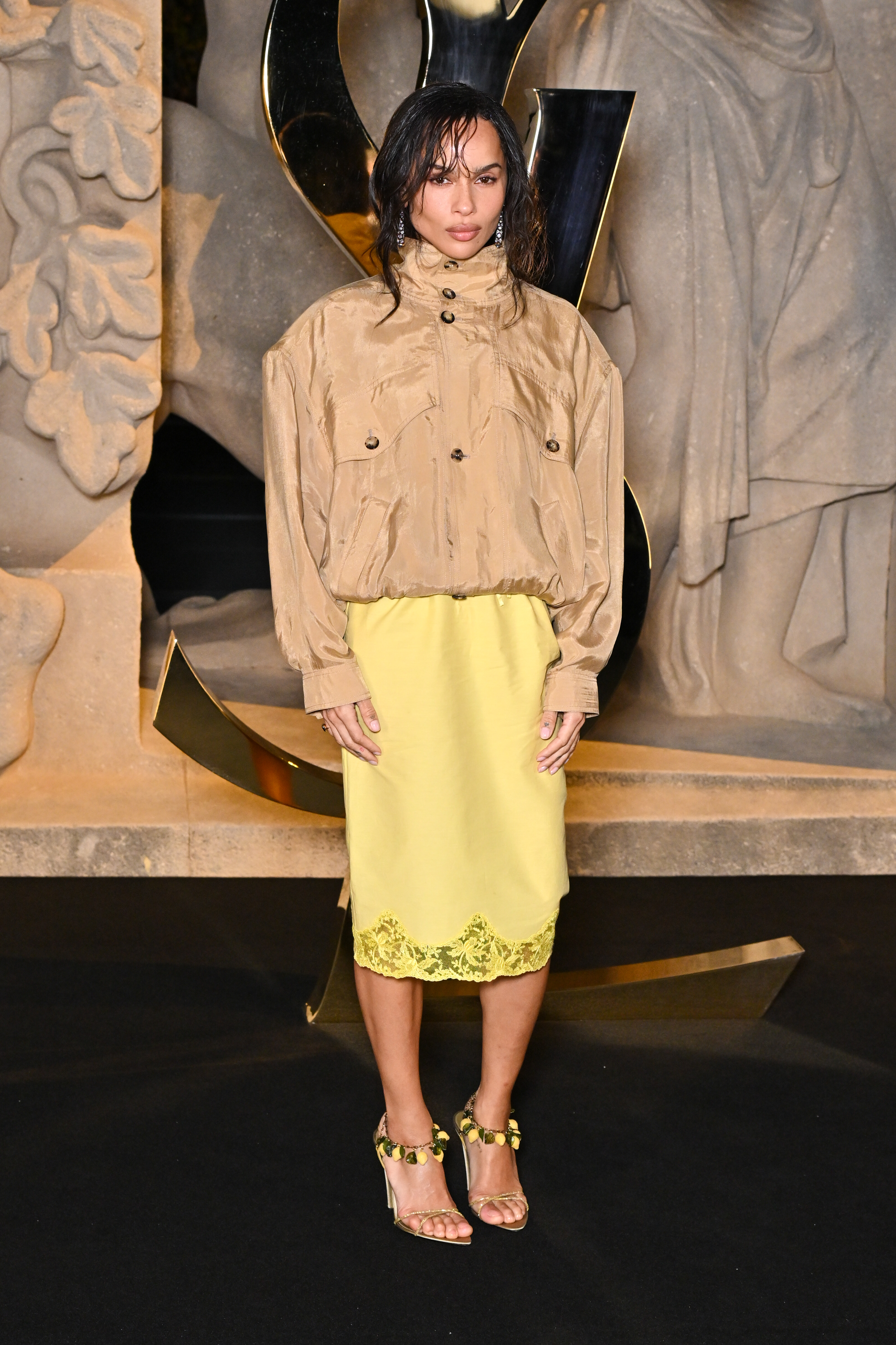 Zoë Kravitz attended the Saint Laurent Women’s Spring/Summer 2026 show at Paris Fashion Week in France, turning heads in a silky slip skirt. She styled it with a beige windbreaker, jewel-embellished strappy sandals, and an eye-catching orange clutch.