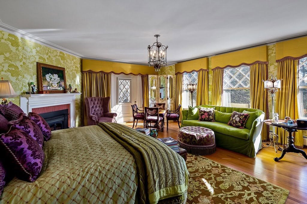 One of the home's 20-plus bedrooms combines green and purple furnishings, floral accents, hardwood floors, and several diamond-pane windows. | Source: Facebook/LegacySIR