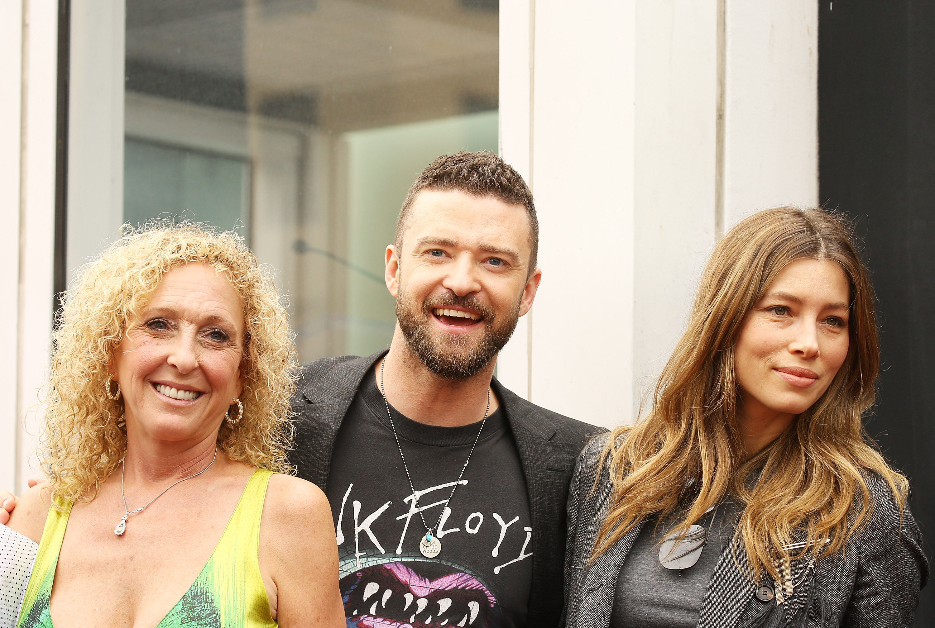 Justin Timberlake poses with Jessica Biel and a woman at an event. Timberlake wears a graphic black T-shirt beneath a gray blazer, while Biel wears a gray top and matching blazer with her long hair styled in loose waves.