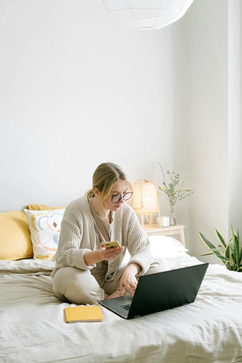 A woman looking at her laptop with her phone in hand | Source: Pexels