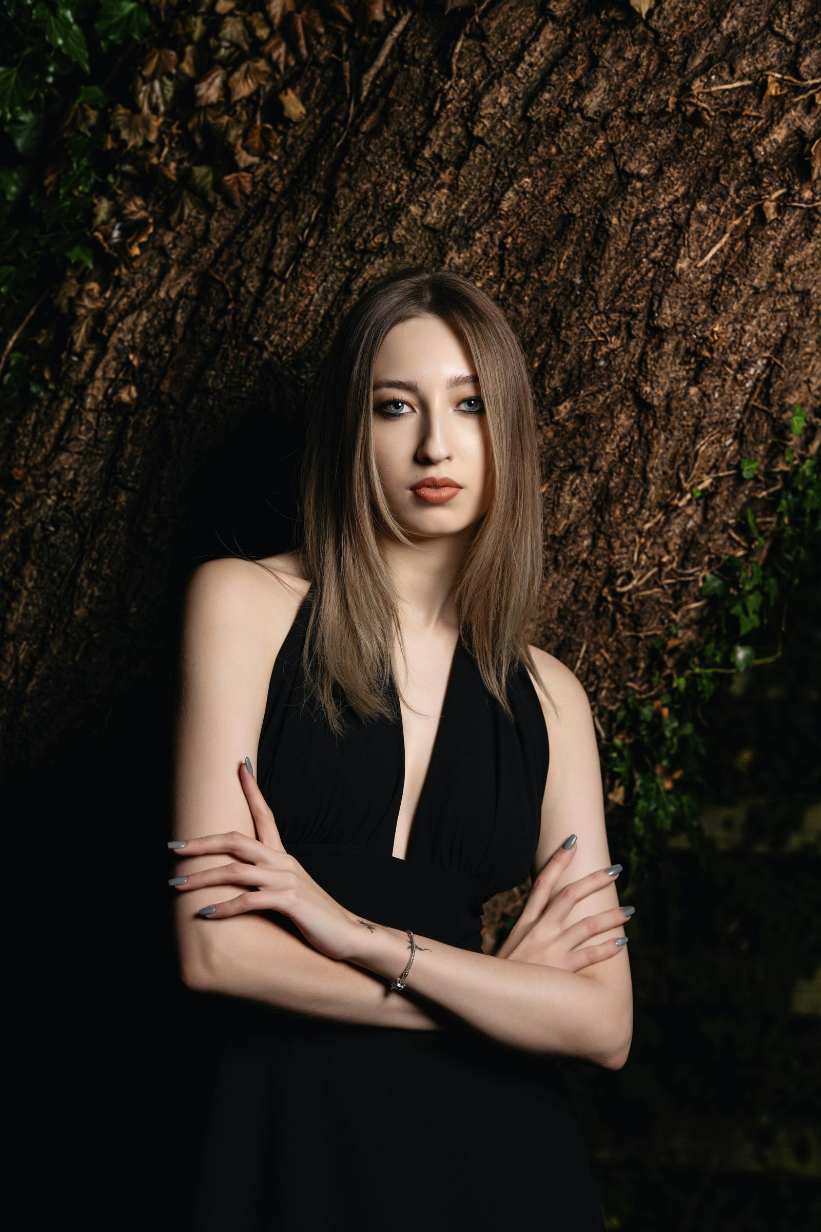 Woman in a black dress standing next to a tree | Source: Pexels