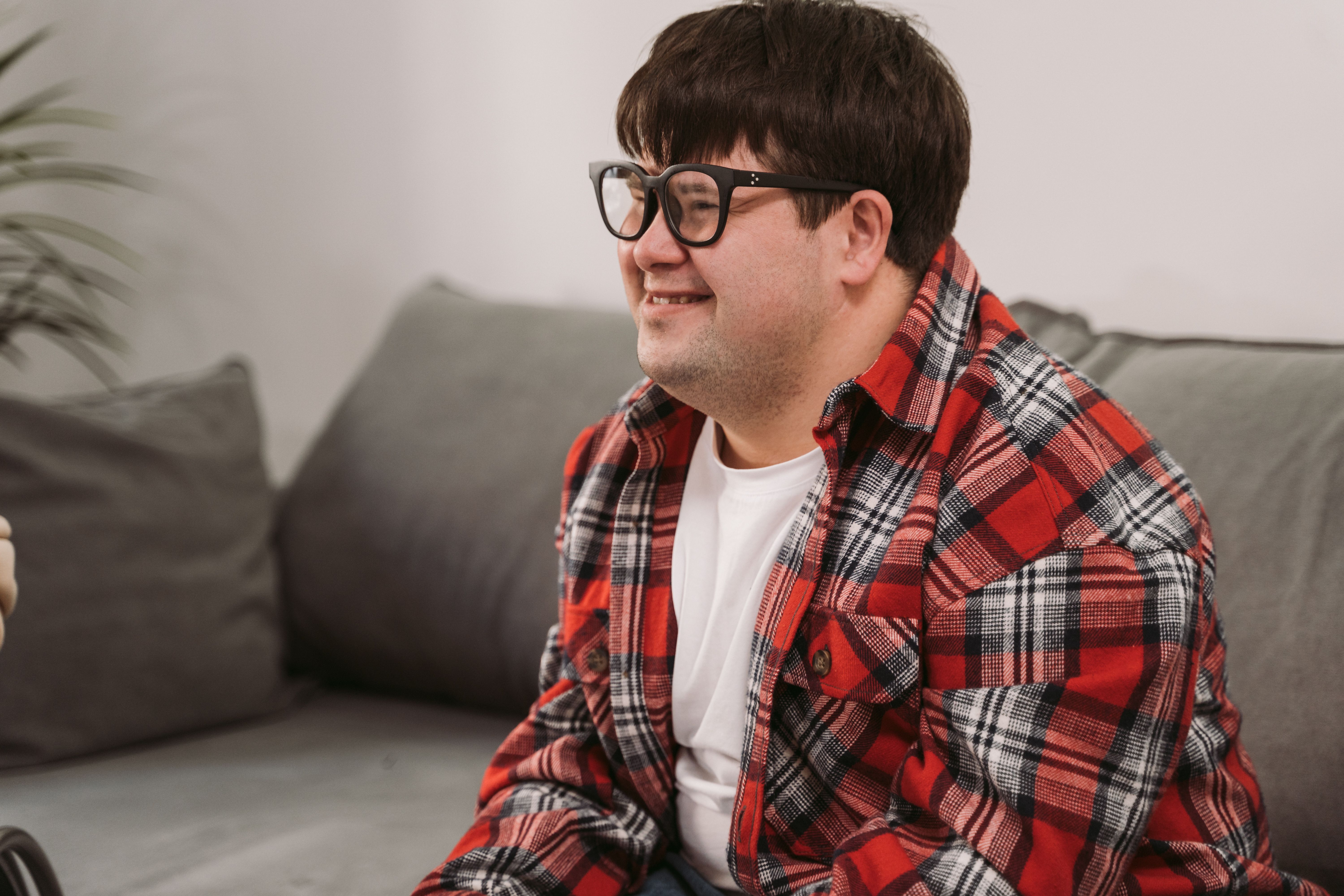 Smiling man in glasses and plaid shirt seated on a cozy couch indoors | Source: Pexels