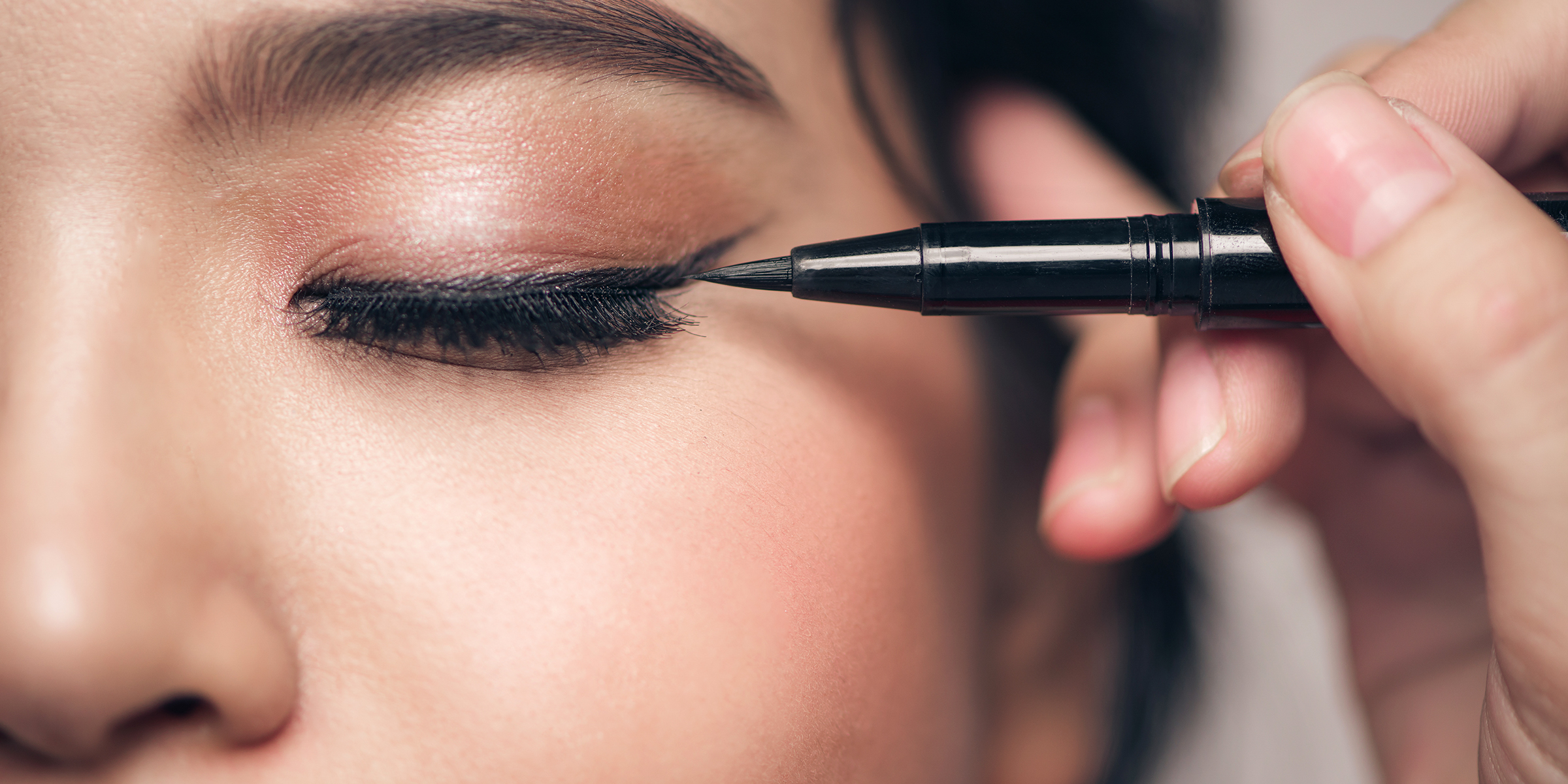 A makeup artist applies eyeliner to a woman's eyelid. | Source: Shutterstock