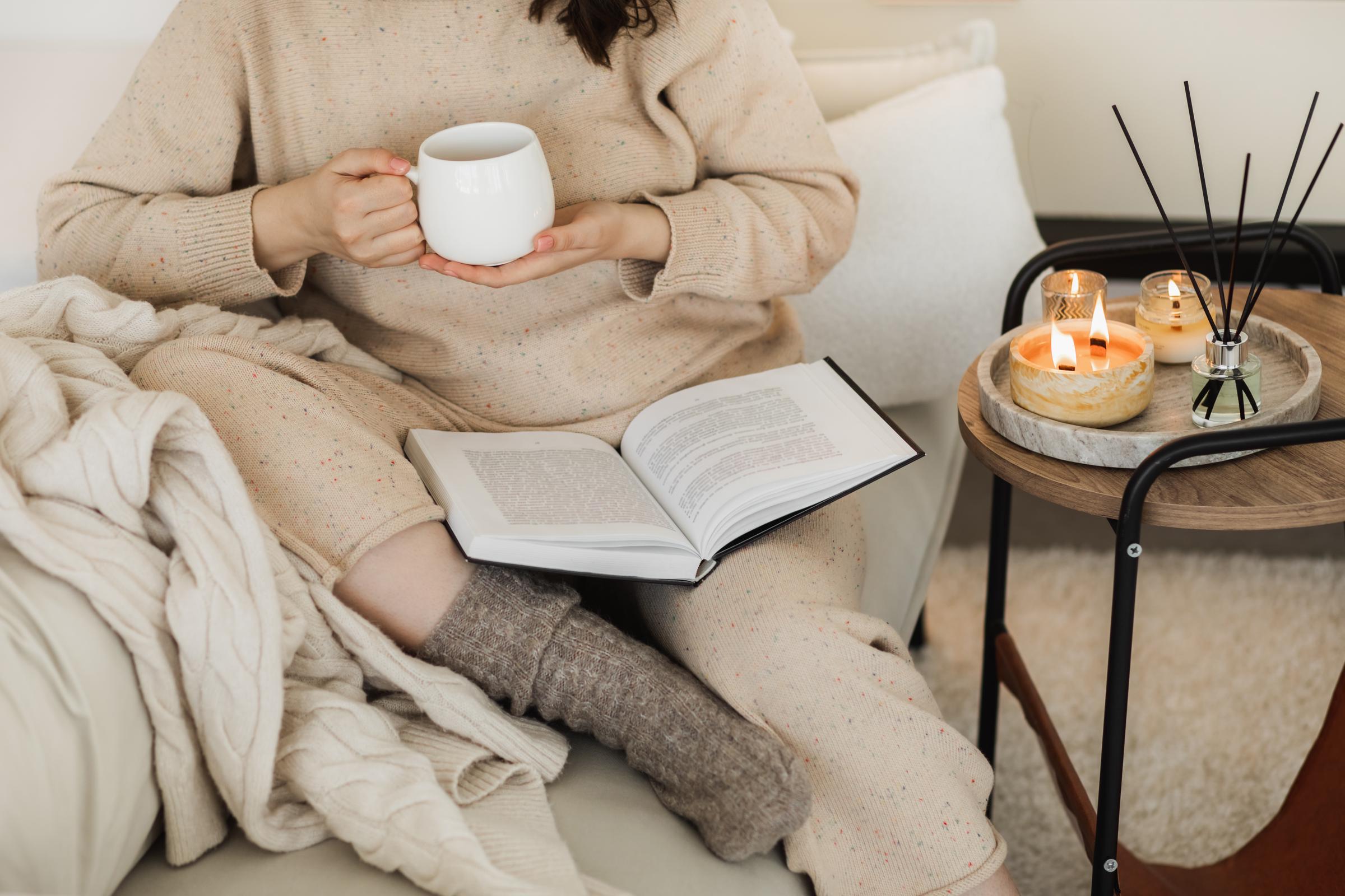A woman with cup of hot coffee sitting on a comfortable couch and reading book in a living room | Source: Getty Images