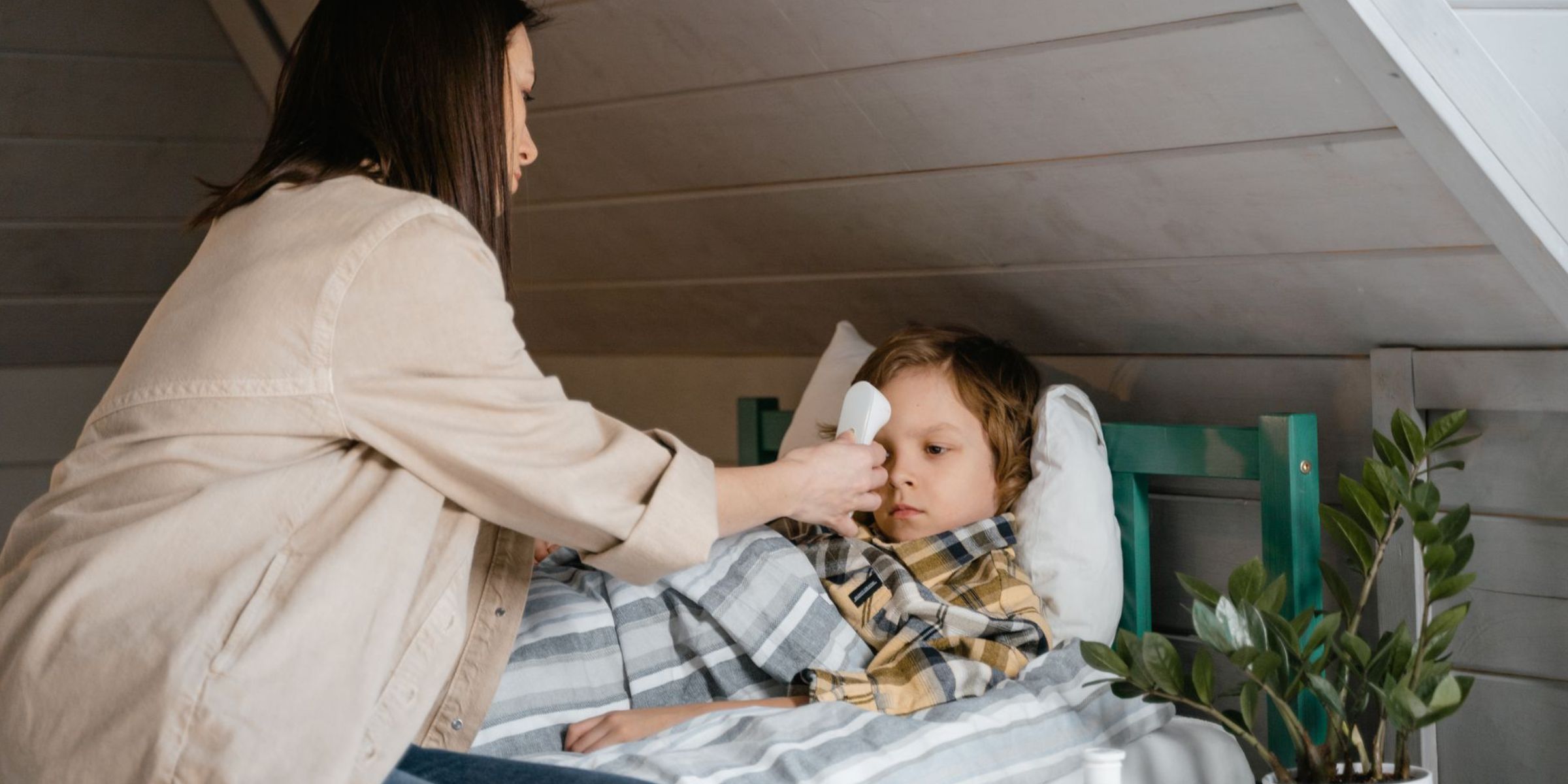 Mother checking her sick child's temperature while he rests in bed | Source: Pexels