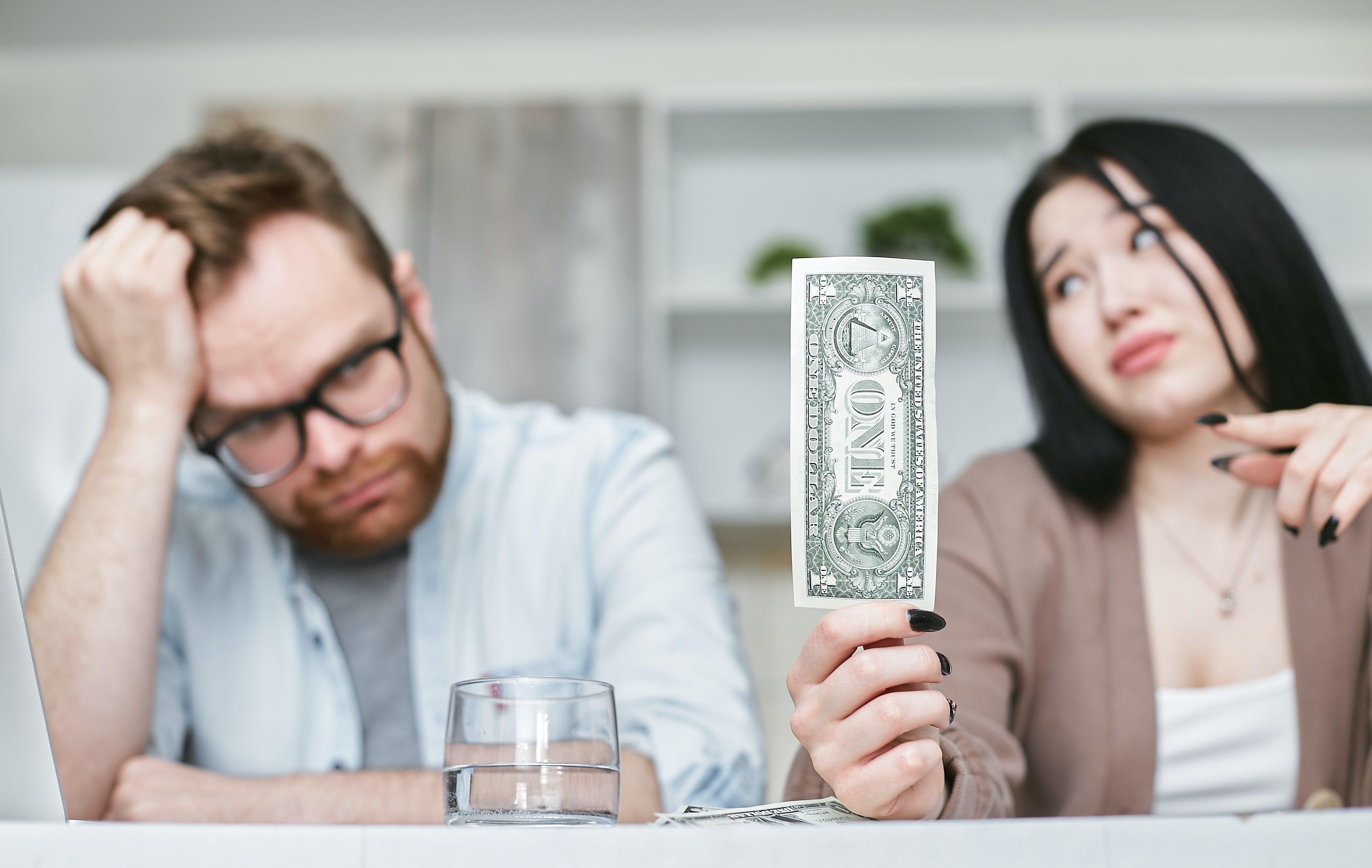 A frustrated couple sitting at the table with the woman holding a dollar bill | Source: Pexels