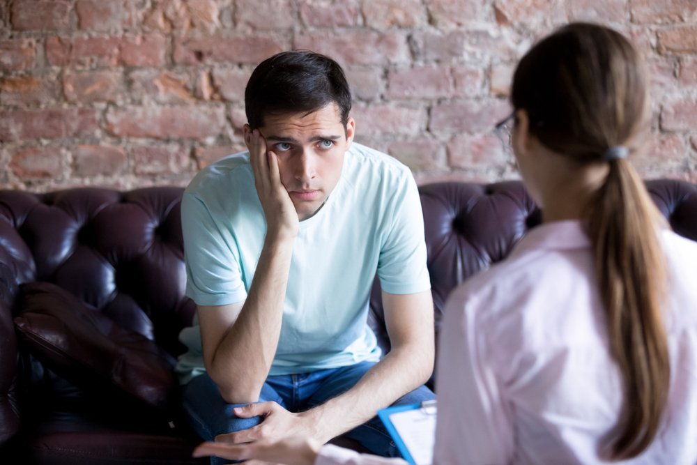 An unhappy male patient balancing his chin on his hand while listening to a psychiatrist for advice | Photo: Shutterstock/fizkes