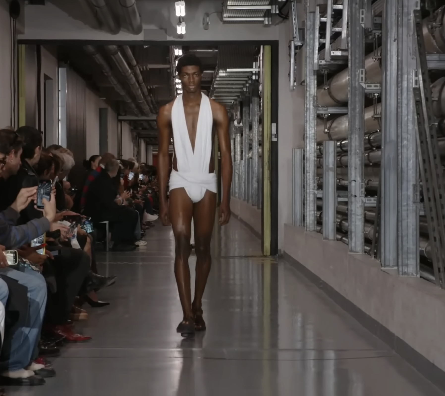 A male model in a cutout bodysuit design. This time in white, glowing strikingly against his dark chocolate skin. The look hinted that futuristic fashion might draw from the past, with a loin section reminiscent of the Roman subligaculum. From a post dated October 5, 2025. Source: Youtube/@jeanpaulgaultier