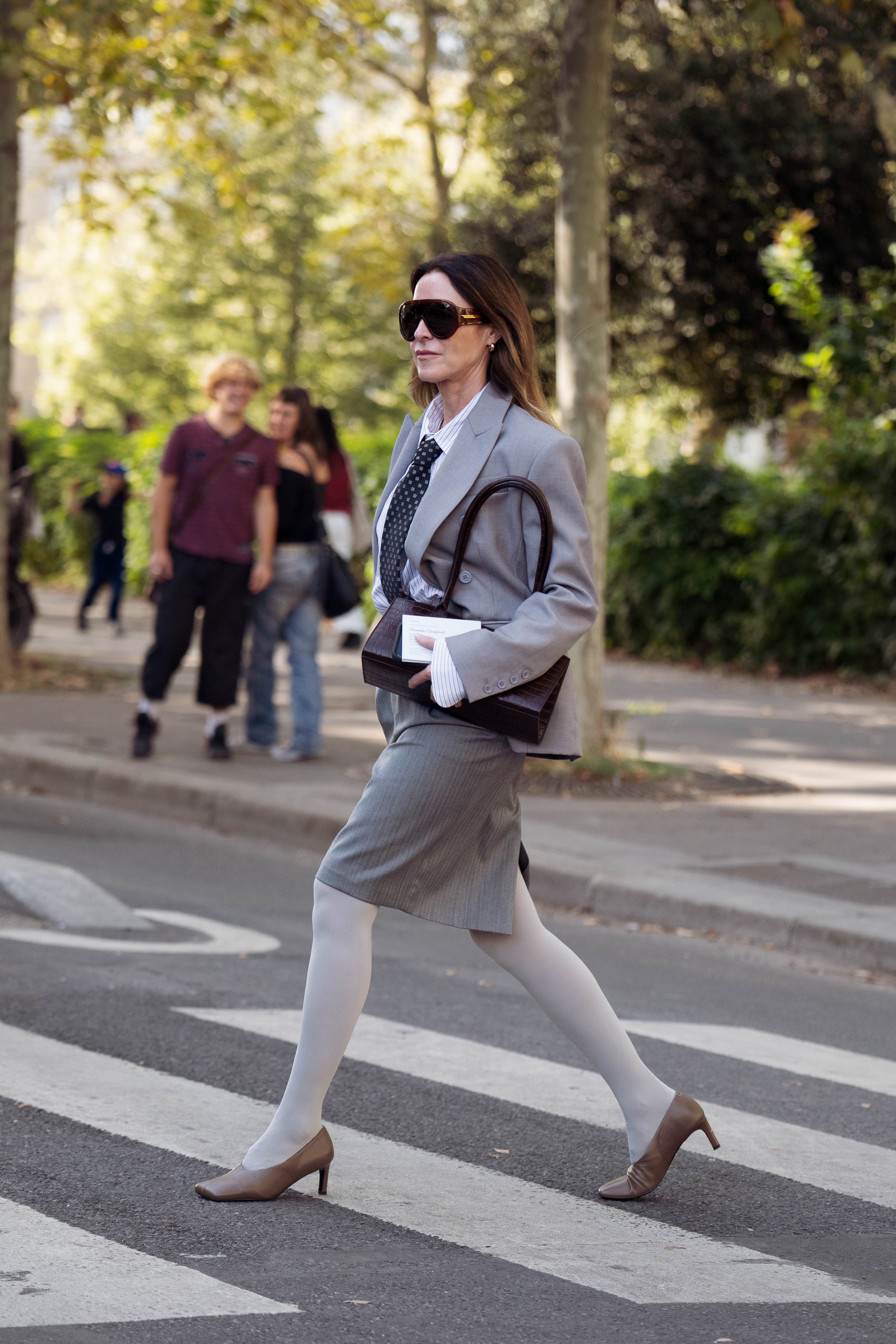 A guest wearing a gray blazer with a gray skirt and white tights crossing the street outside the Hermes show during Paris Fashion Week on October 3, 2026 | Source: Getty Images