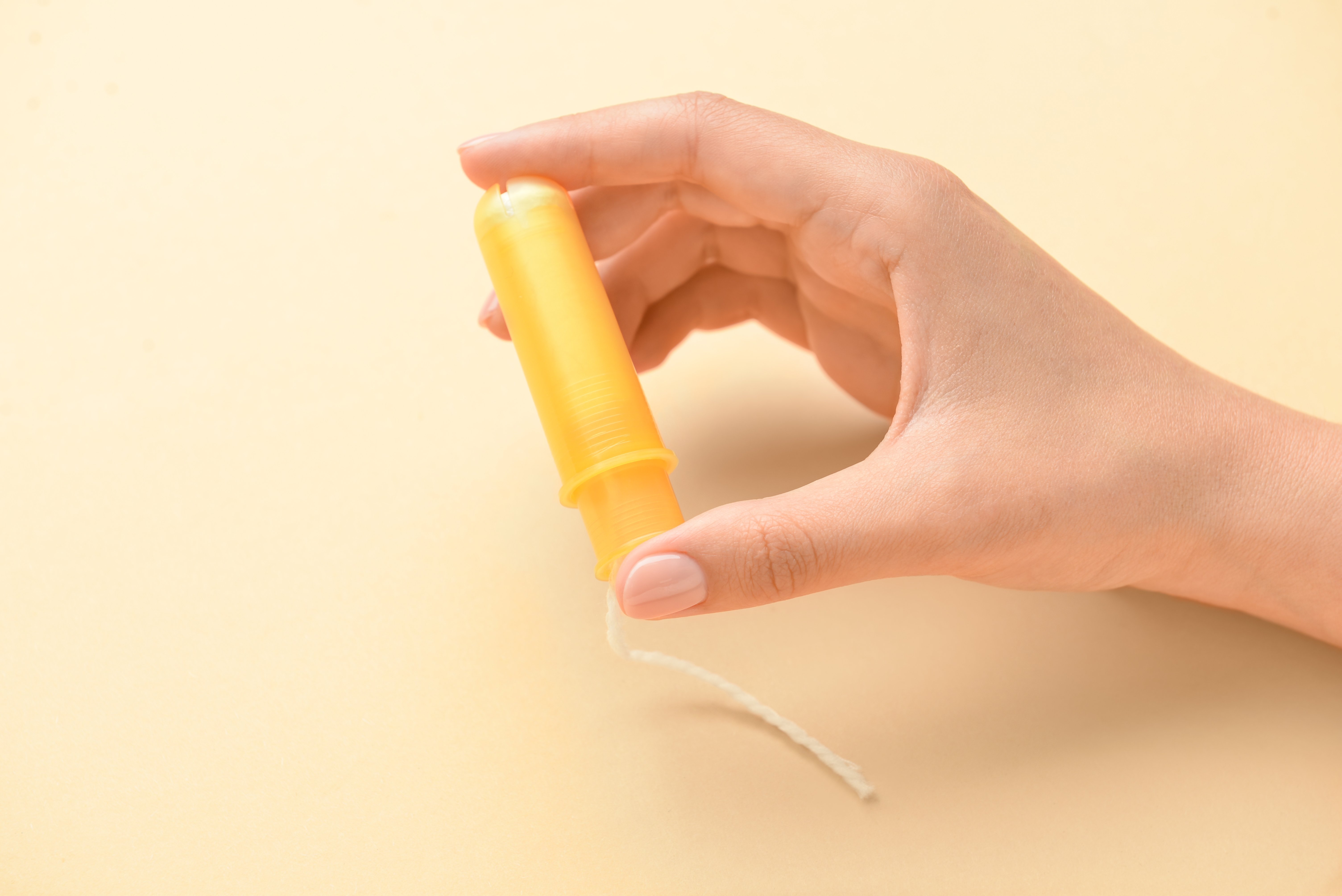 A woman showing a piece of sanitary tampon with yellow plastic applicator. | Source: Shutterstock