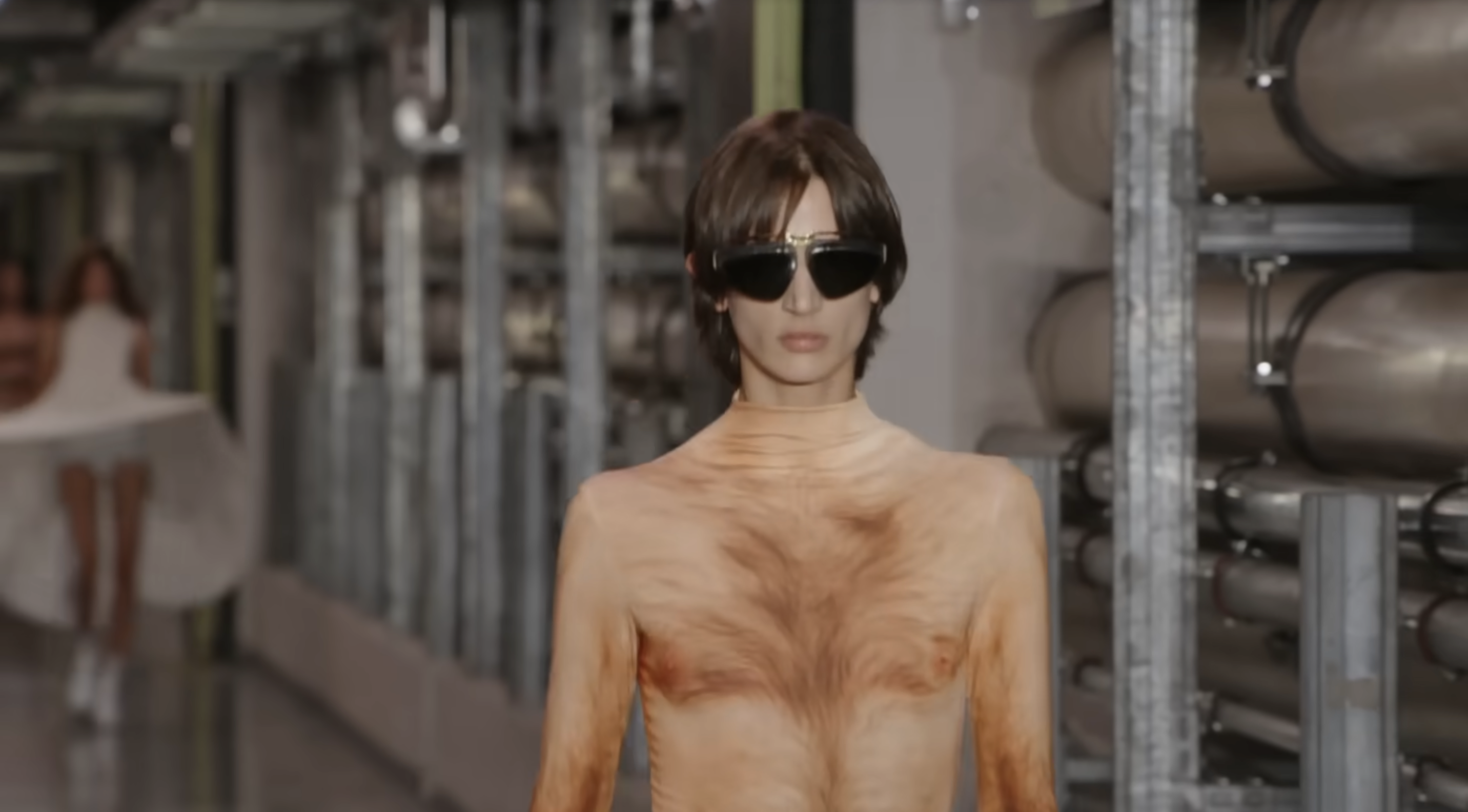 However, a closer camera shot revealed that the model was actually wearing a jumpsuit beneath the skirt. The piece matches his skin tone and features a printed body-hair design that creates the illusion of bare skin. From a post dated October 5, 2025. Source: Youtube/@jeanpaulgaultier