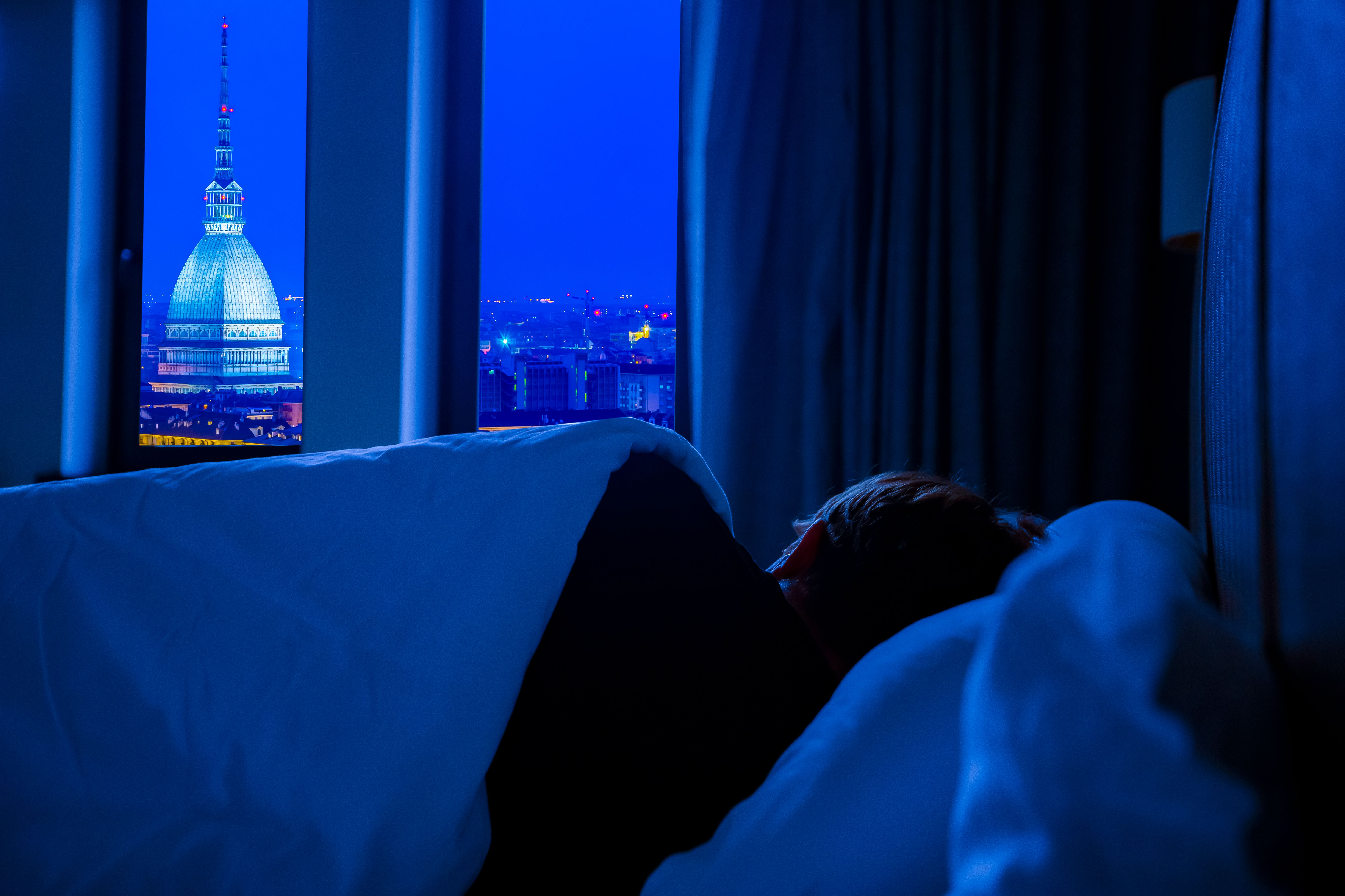A person asleep in bed by an open window, with city lights shining in at night | Source: Pexels