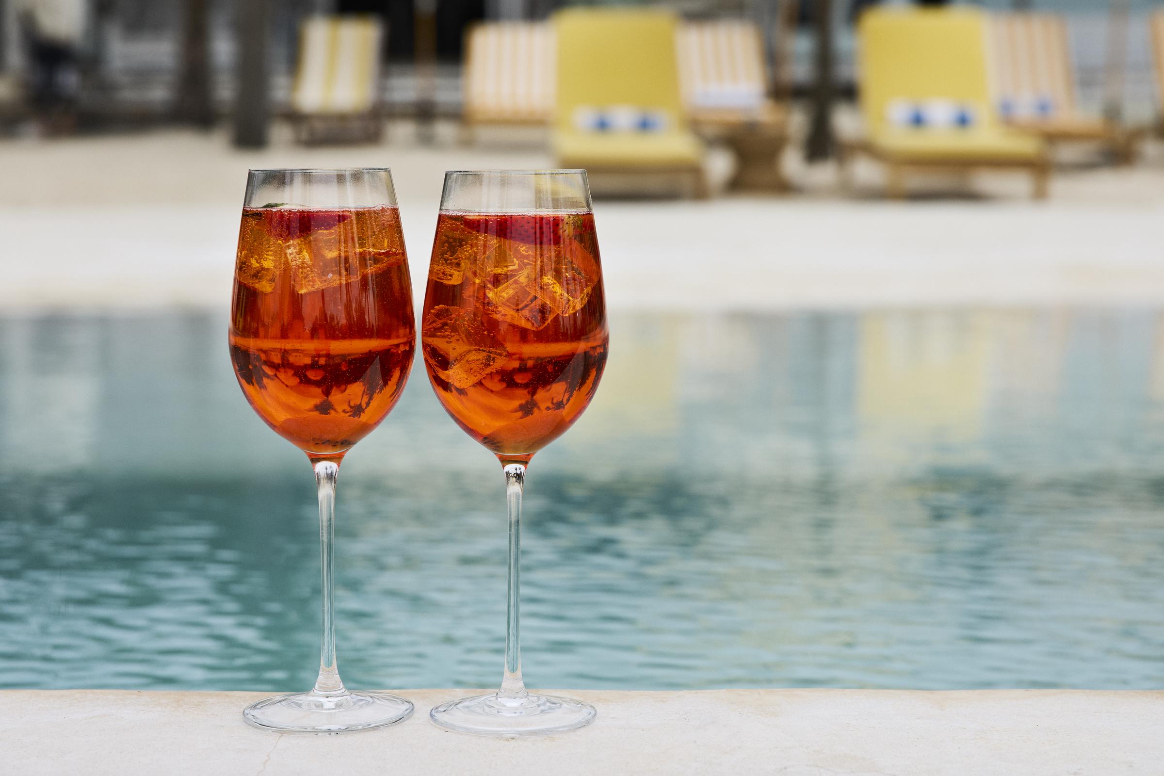 A pair of tall stemmed Aperol Spritz cocktails kept on the ledge of a swimming pool | Source: Getty Images