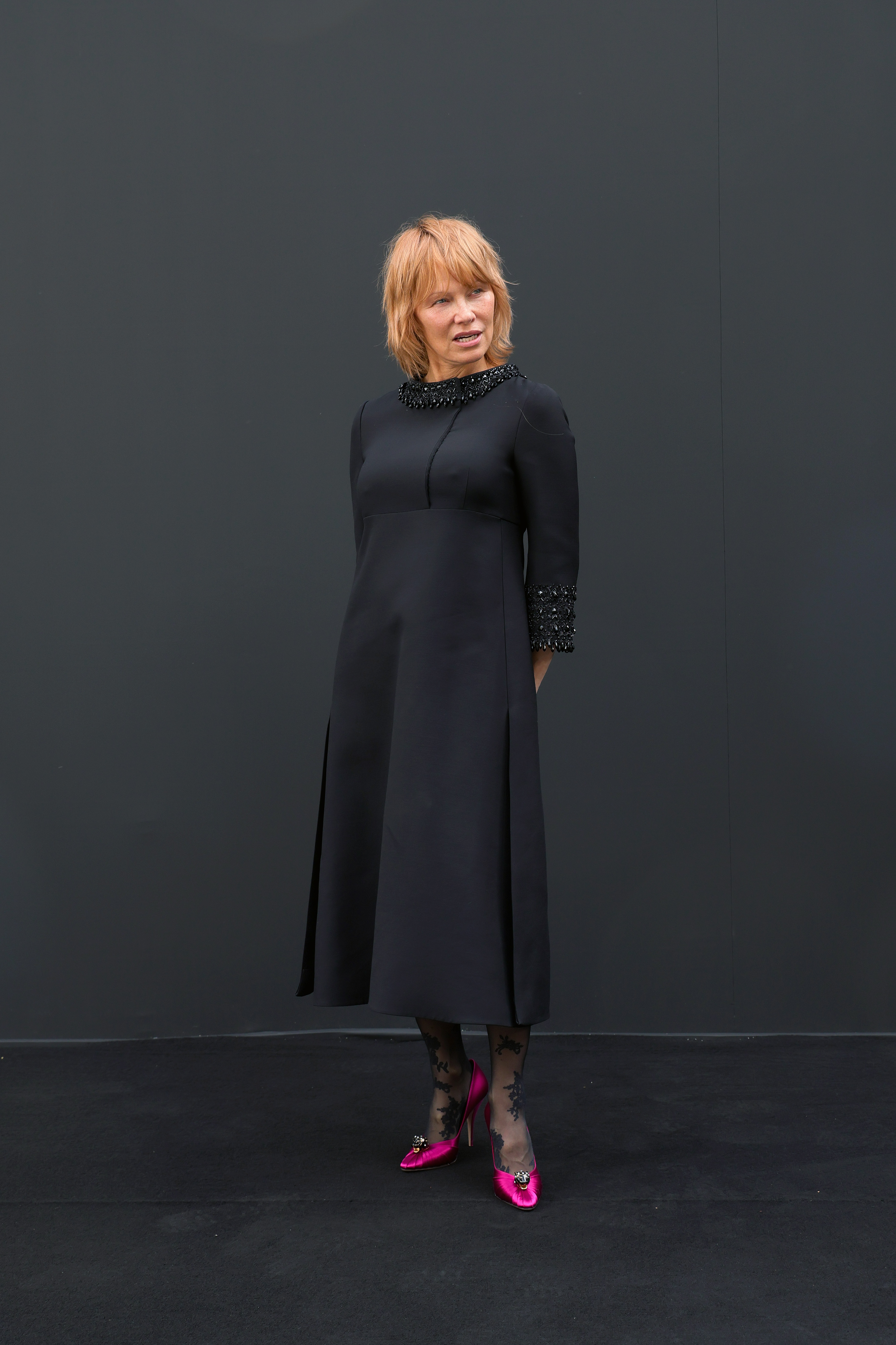 Pamela Anderson attended the Valentino show at Paris Fashion Week in France, exuding sophistication in a black boat-neck midi dress with a sequined collar and cuffs. She paired the look with patterned sheer tights and bright pink satin heels adorned with a sparkling brooch.