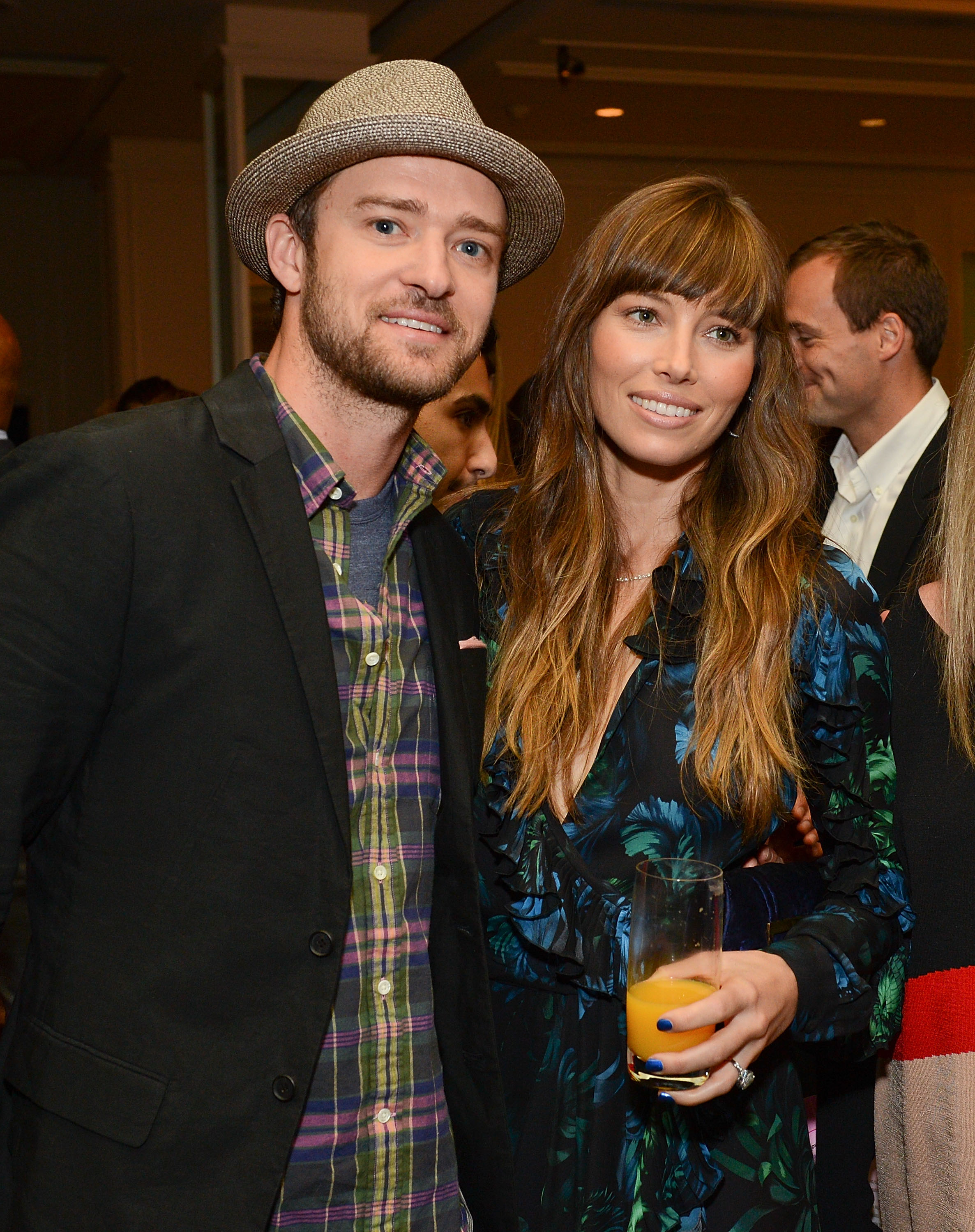 Justin Timberlake and Jessica Biel pose together at an event, smiling for the camera. Timberlake wears a gray fedora over a plaid shirt and dark blazer, while Biel sports a blue-and-black patterned dress with her long hair styled in loose waves. | Source: Getty Images