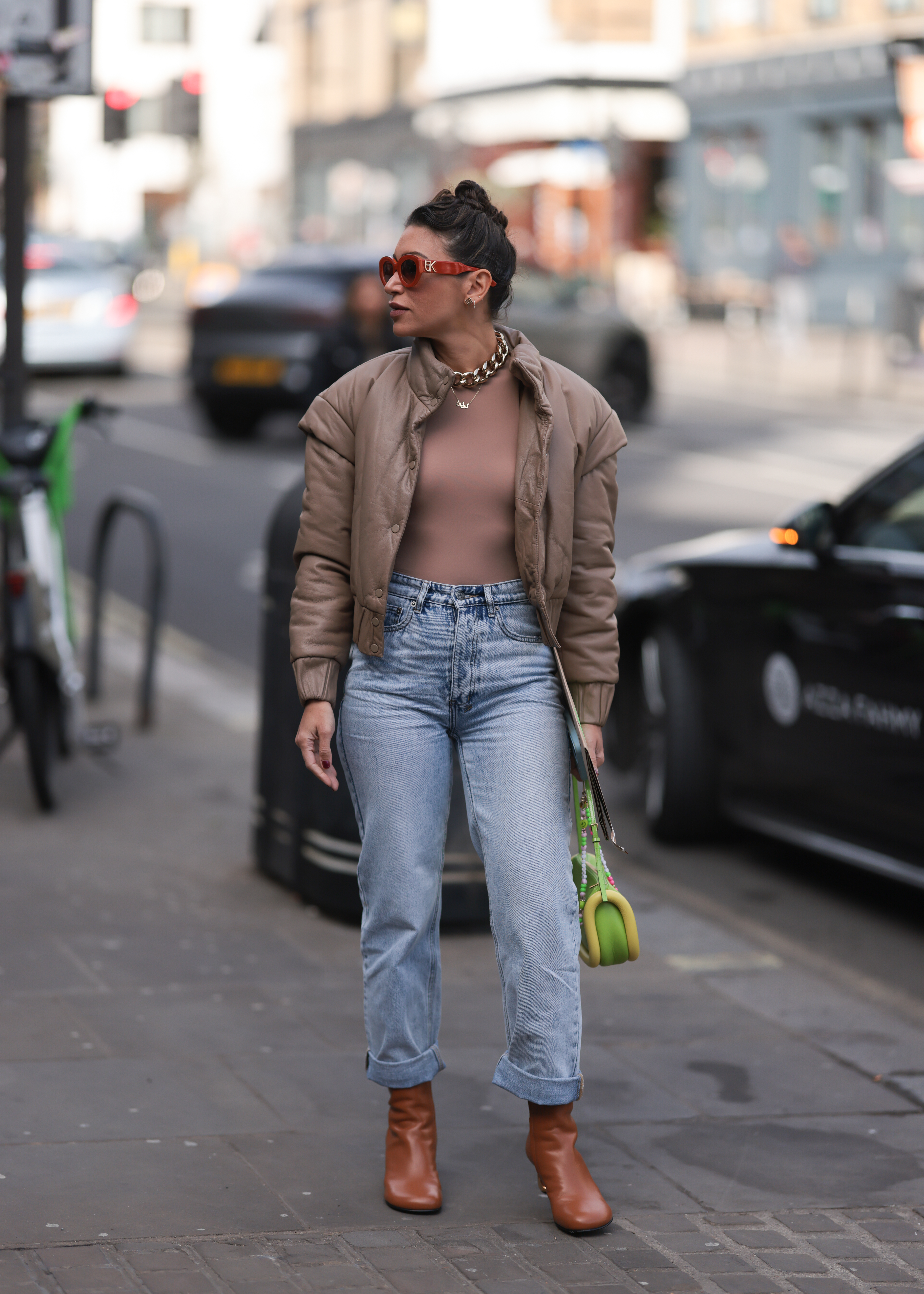 A fashion week guest pairing her blue mom jeans with shades of brown and green during London Fashion Week on February 19, 2023, in London | Source: Getty Images