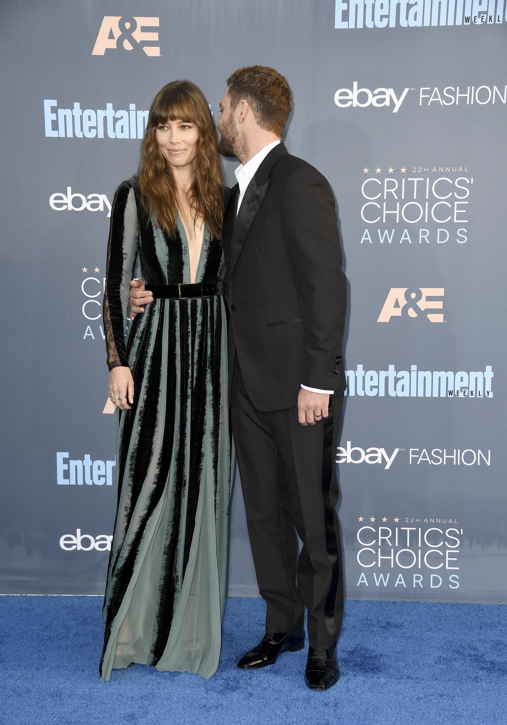Justin Timberlake leans toward Jessica Biel as they pose at the Critics' Choice Awards. Biel wears a floor-length teal-and-black striped gown with sheer sleeves, while Timberlake looks sharp in a black suit and white shirt.