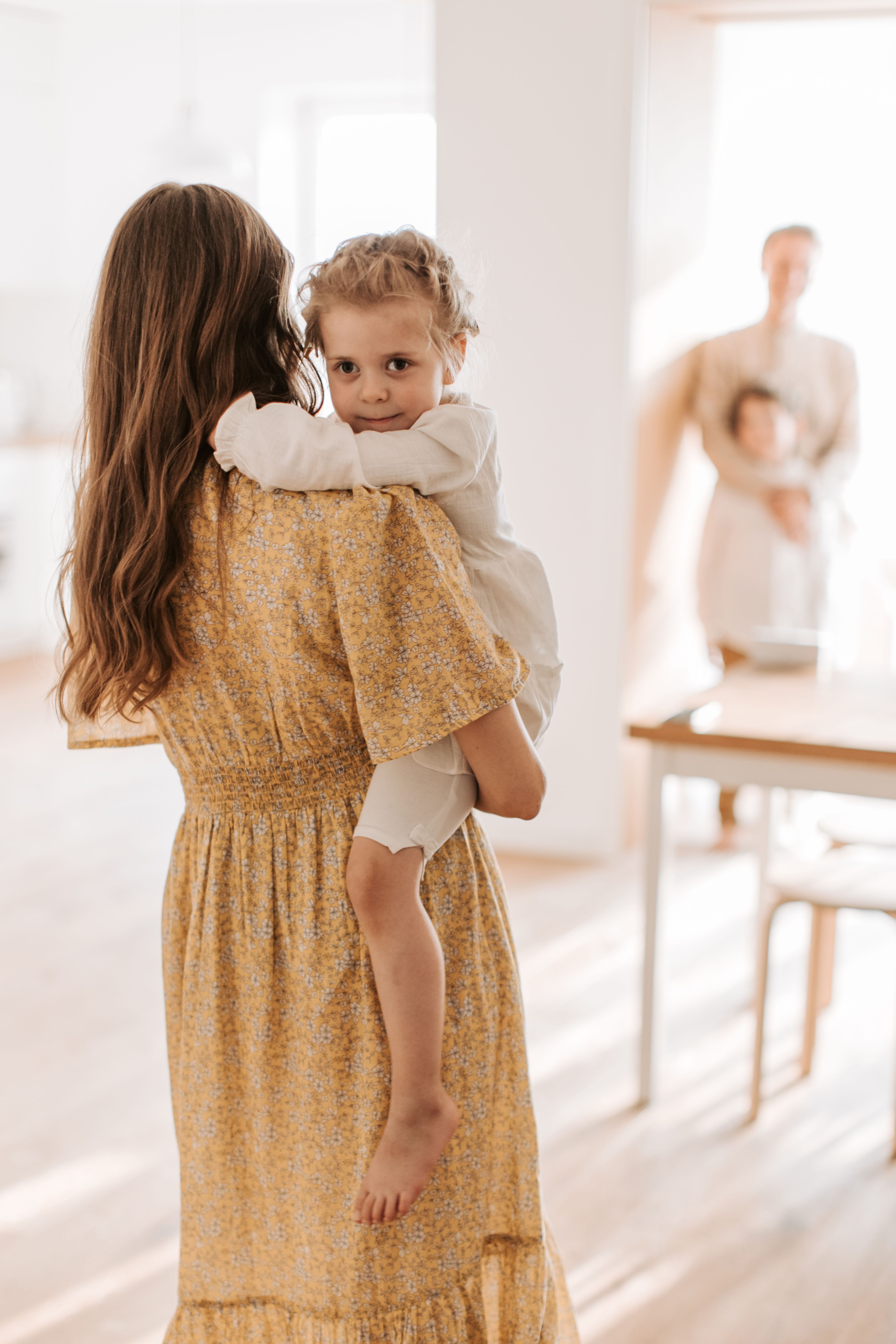 A mother holding one child while the father holds another in the background | Source: Pexels
