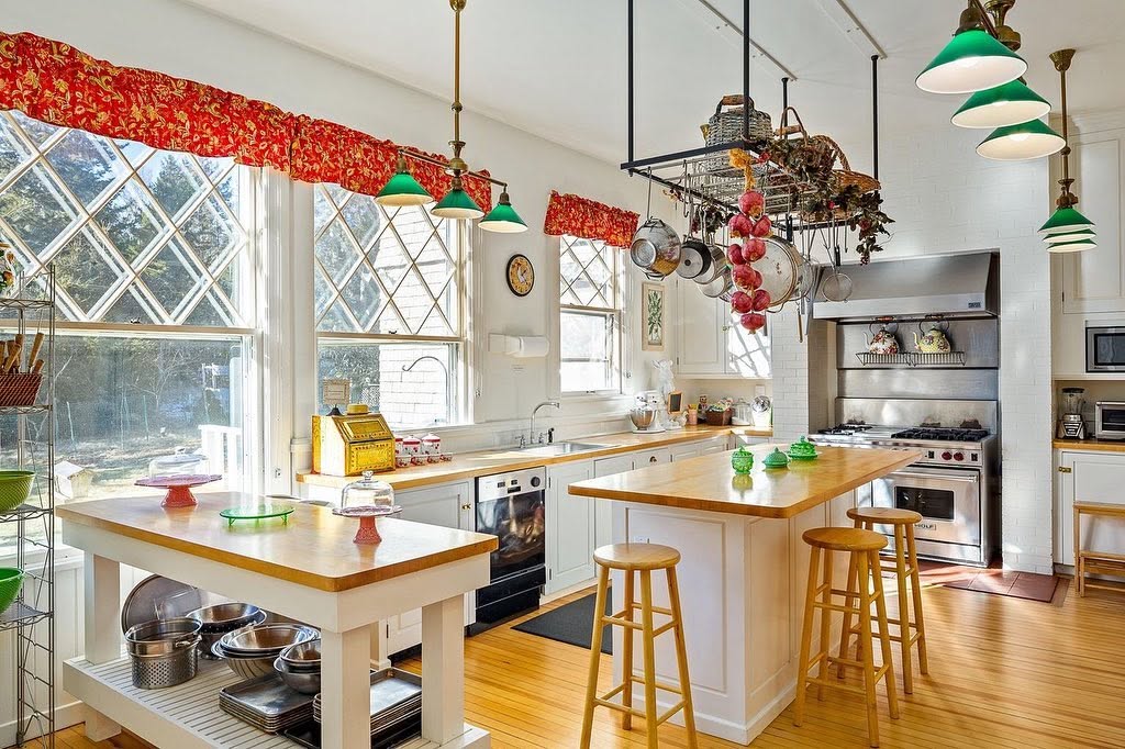The spacious kitchen combines white cabinetry, butcher-block surfaces, two islands, hanging cookware, and commercial-style appliances. | Source: Facebook/LegacySIR