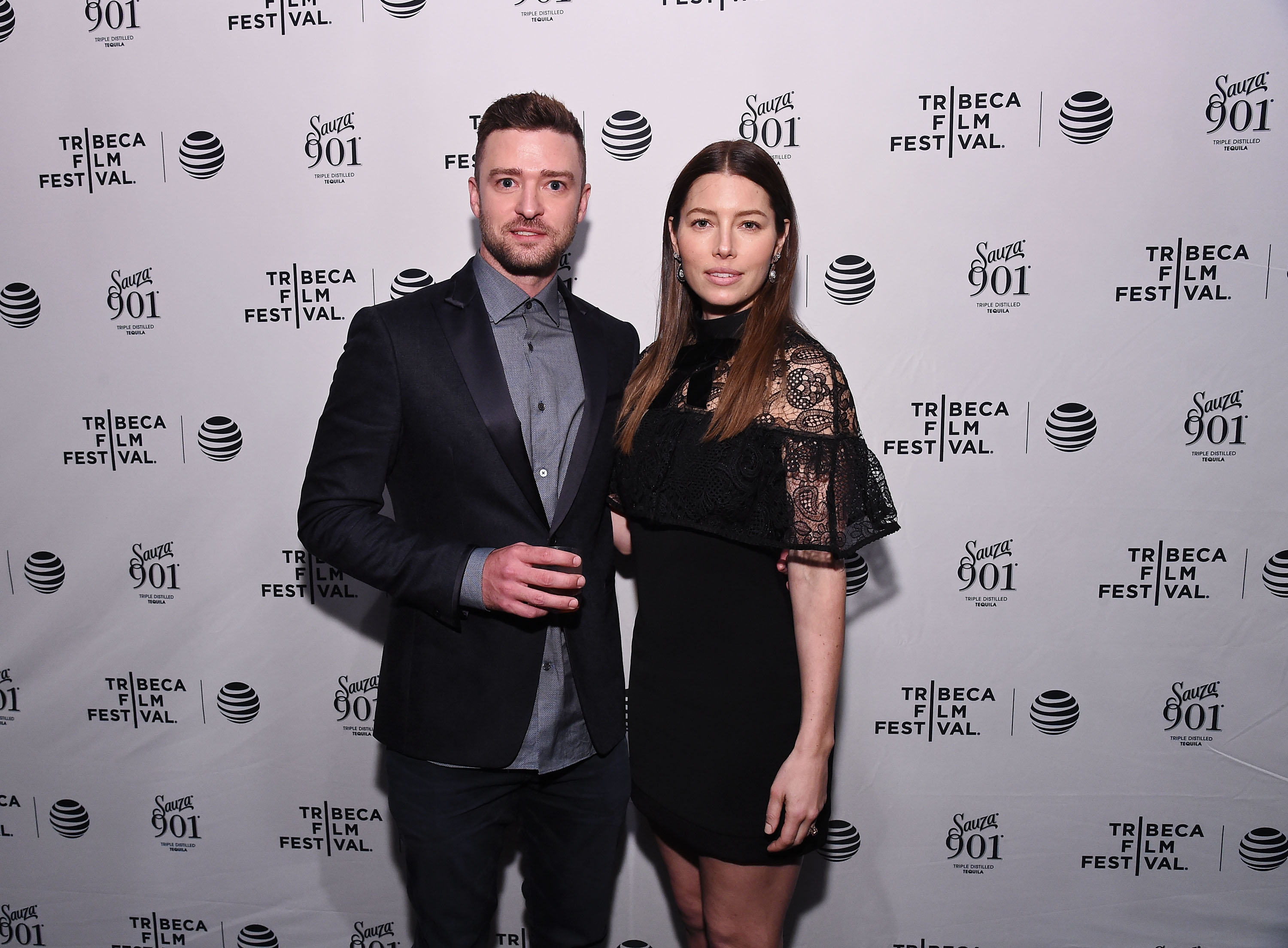 Justin Timberlake and Jessica Biel pose on the red carpet at the Tribeca Film Festival. Timberlake wears a dark suit over a gray shirt, while Biel pairs a black mini dress with a lace cape-style overlay.