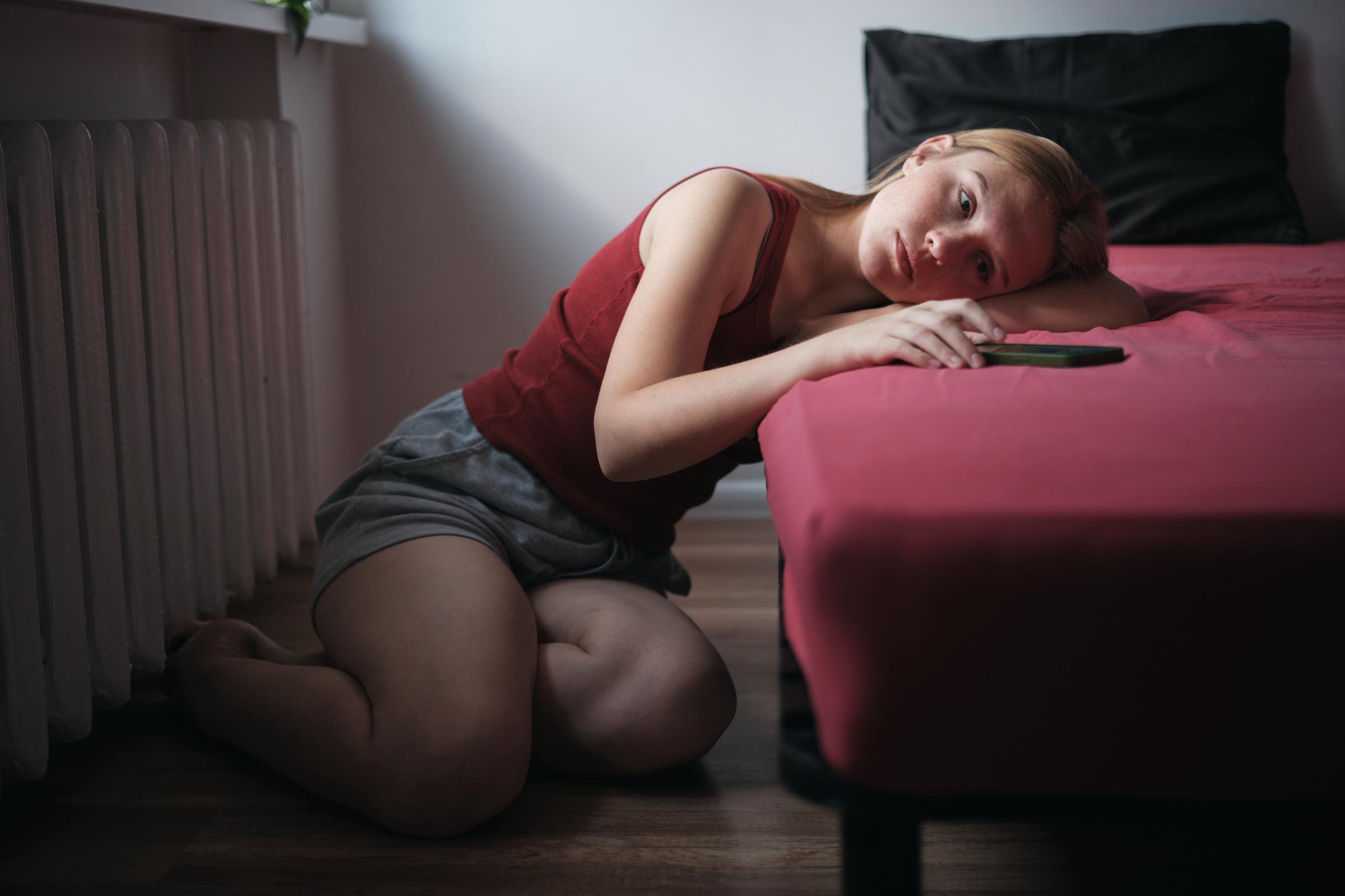 A solemn-looking woman sitting on the floor on the side of her bed | Source: Getty Images