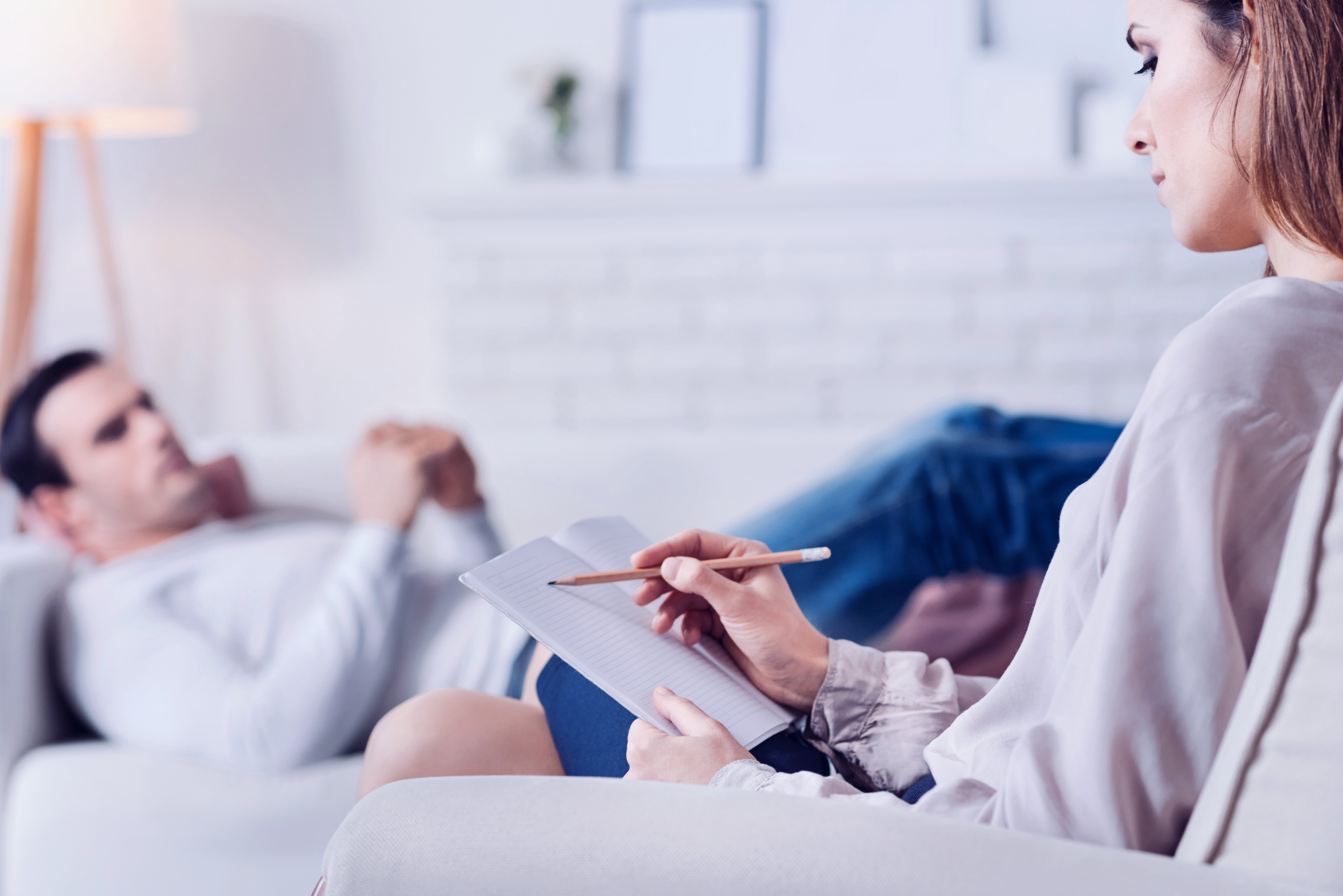 A professional psychologist taking notes while speaking to a client who is lying on a couch | Photo: Shutterstock/Dmytro Zinkevych