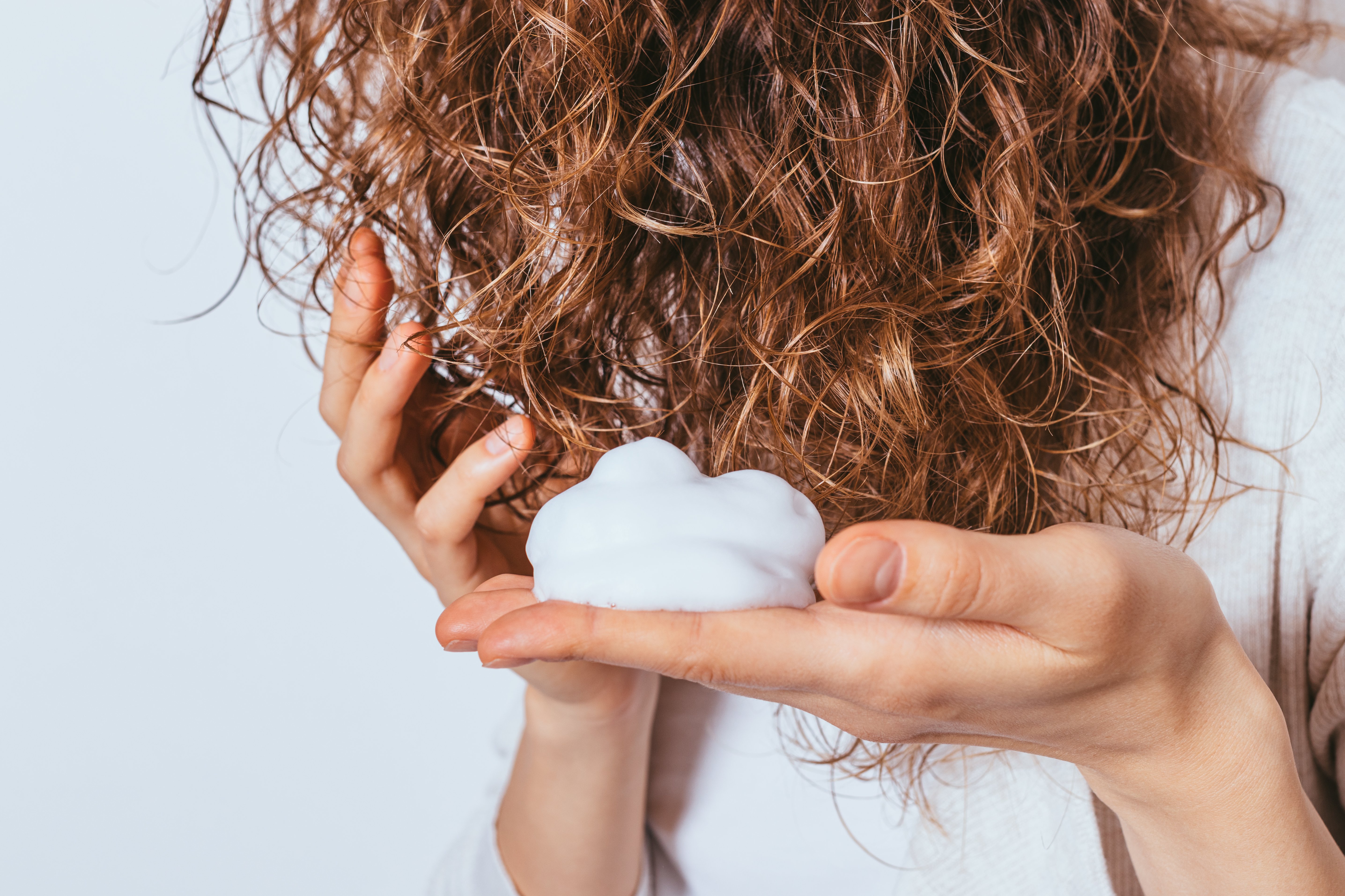 A woman with curly hair applying hair mousse | Source: Shutterstock