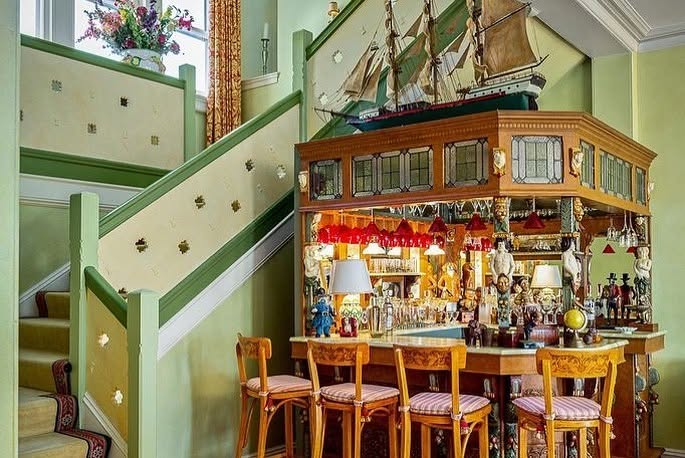 A model sailing ship crowns an elaborate built-in bar tucked beside the staircase, adding a nautical touch to the historic island home. | Source: Facebook/LegacySIR