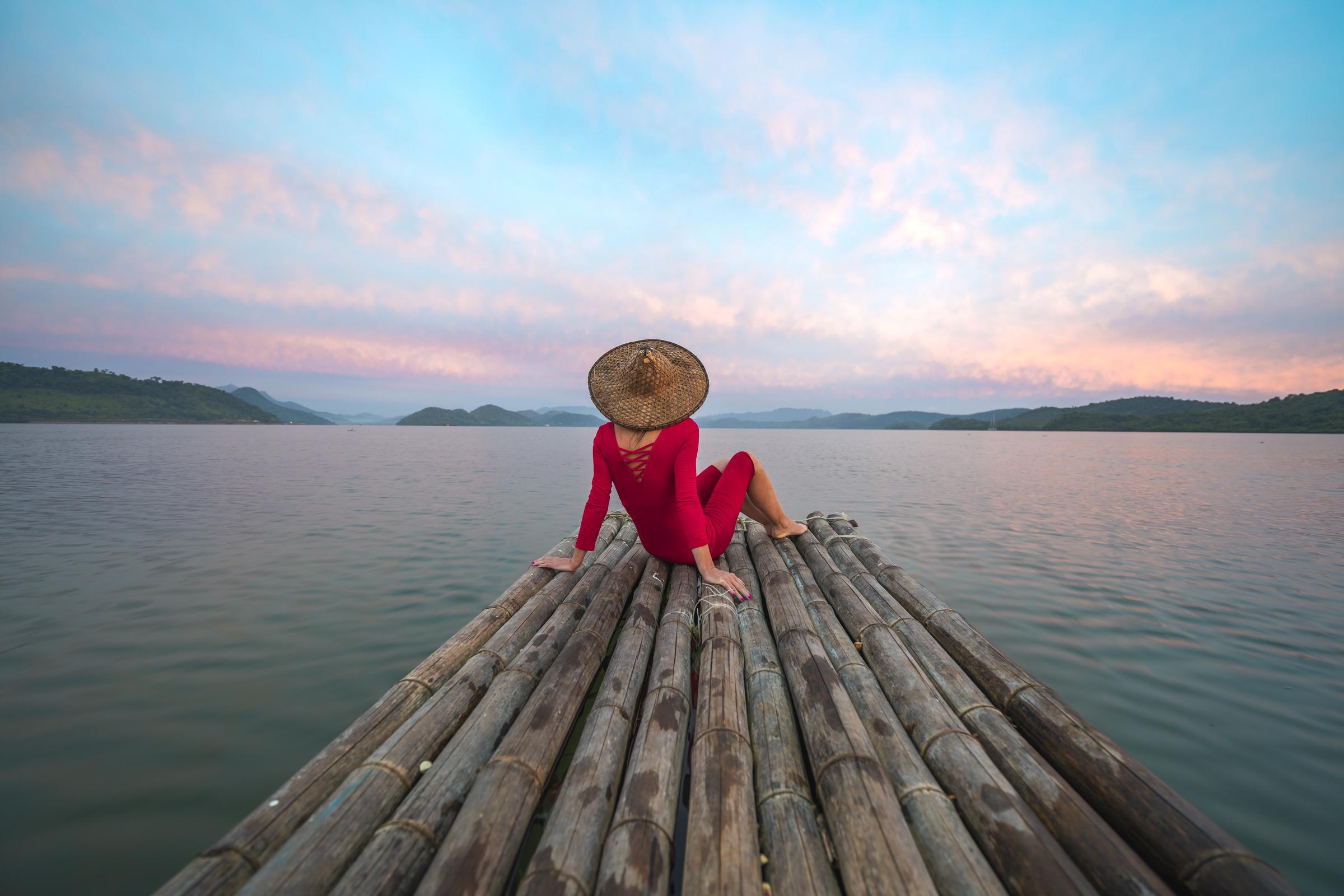 Woman with red dress and traditional hat sitting on a wooden raft | Source: Getty Images