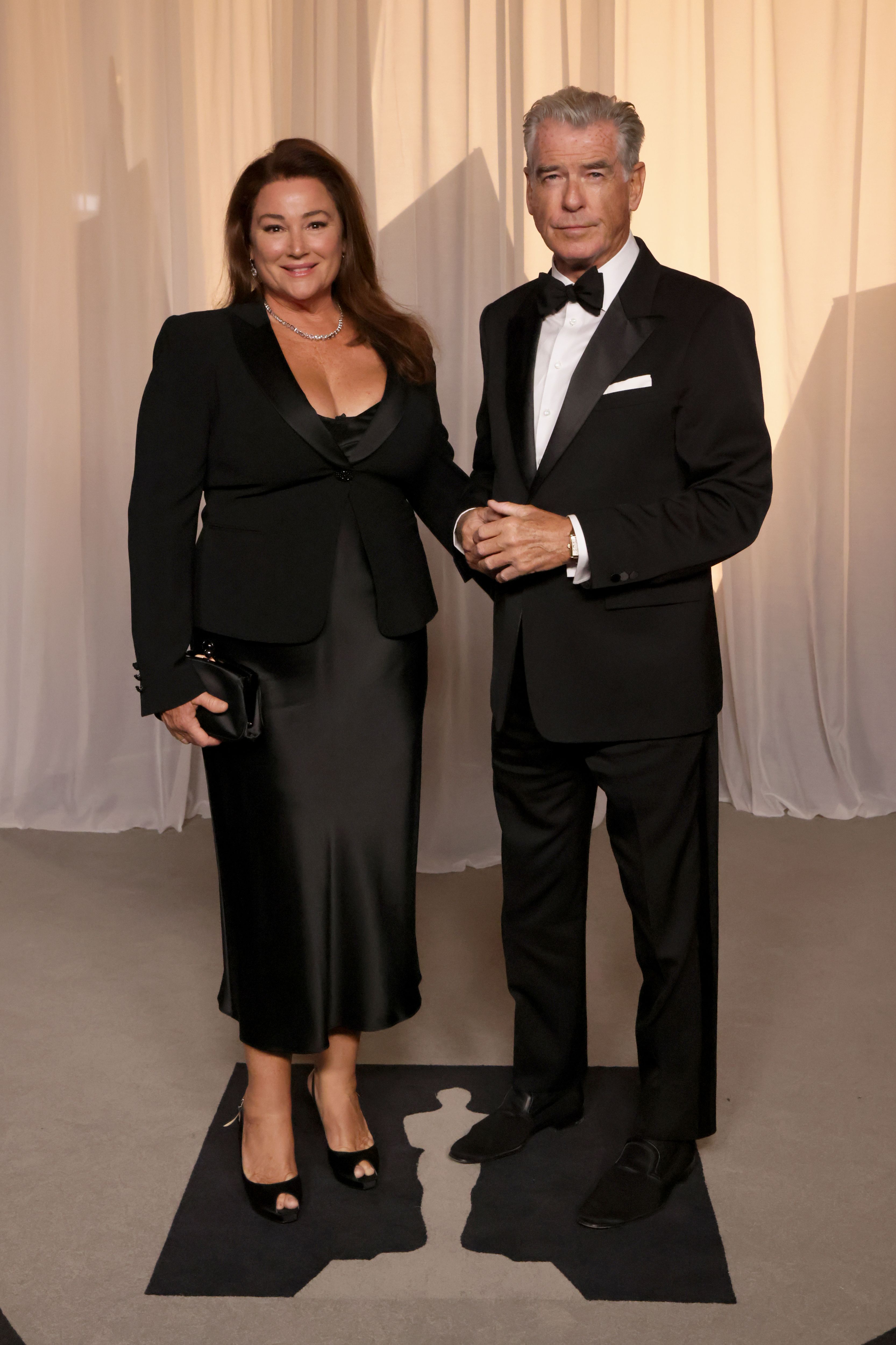 Smith carries a black clutch while standing beside Brosnan for another portrait at the Academy Museum Gala, where he wears a classic tuxedo with a bow tie and white pocket square.