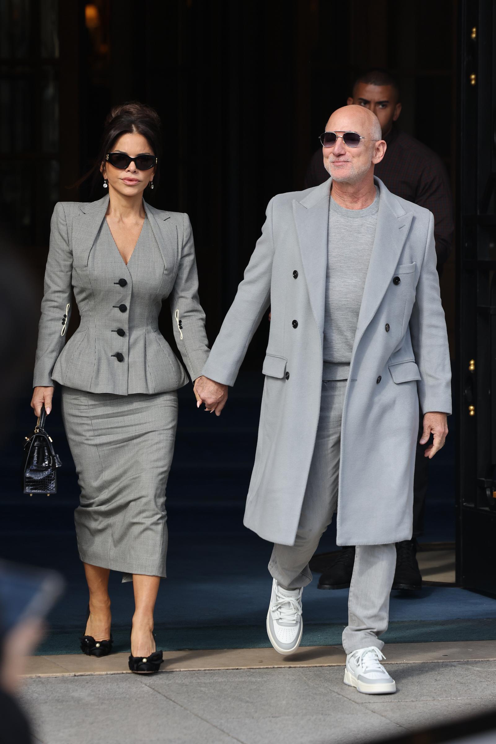 Lauren Sánchez and Jeff Bezos were seen leaving The Ritz during the Women’s Spring/Summer 2026 shows at Paris Fashion Week in France. Bezos kept it casual in a T-shirt and jeans layered under a pocketed coat, paired with sunglasses and sneakers. Lauren wore a checkered suit with a peplum blazer and pencil skirt, and both completed their looks with dark sunglasses.