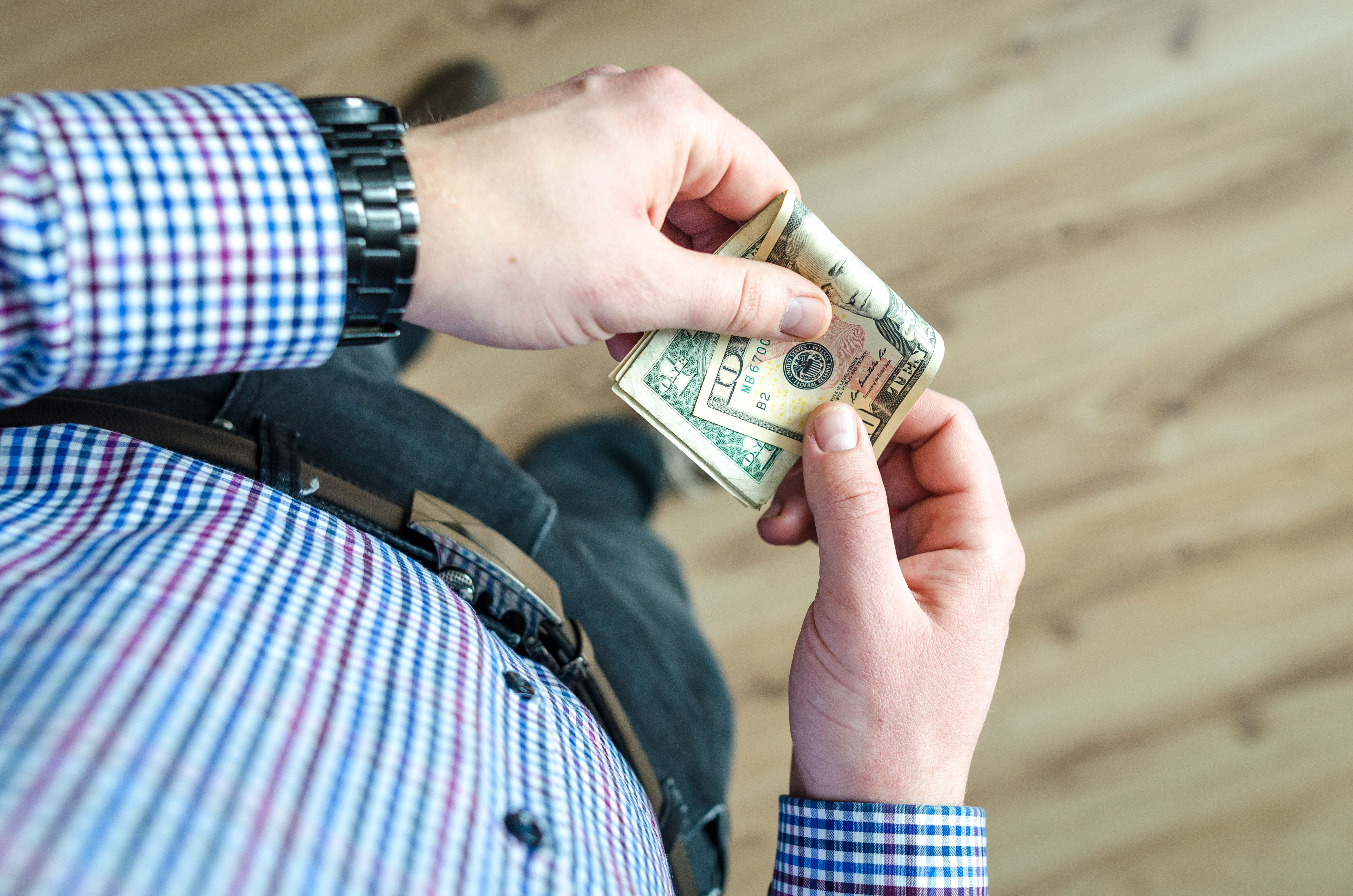 The focus is on a casually dressed man holding US dollar bills in his hands | Source: Pexels