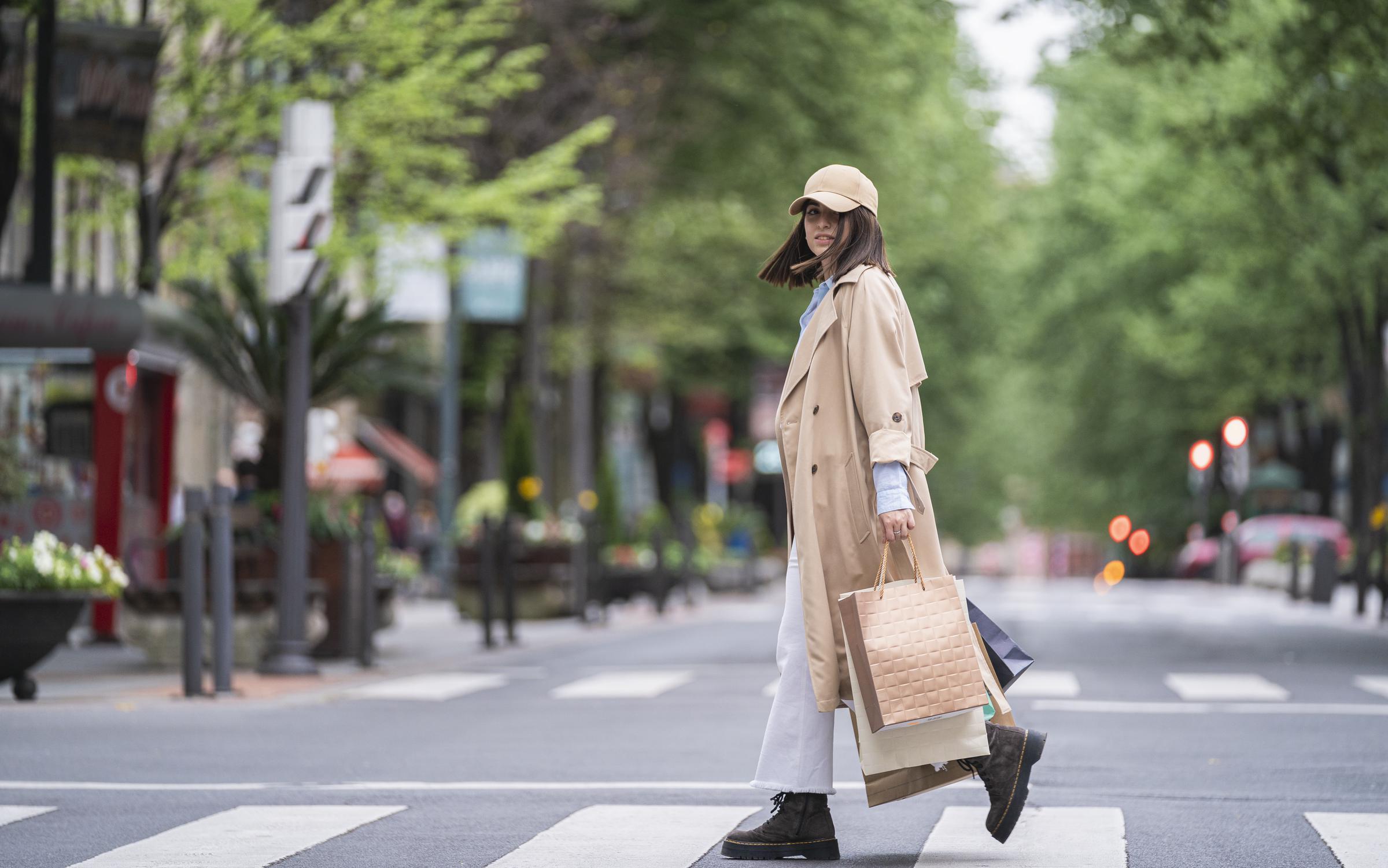 A woman wearing a trench coat crossing the road with shopping bags | Source: Getty Images