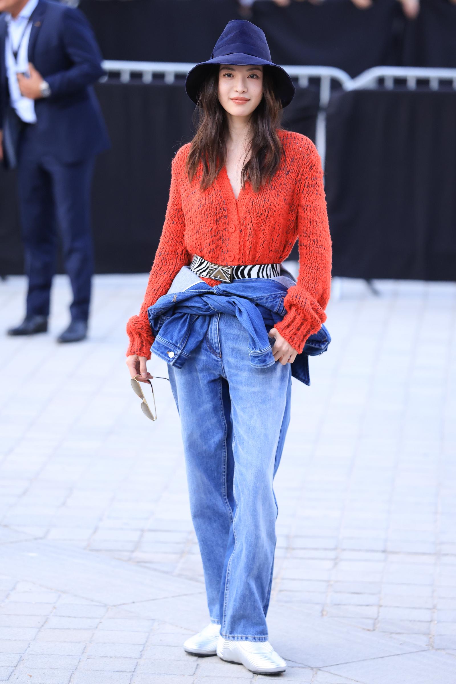 Elaine Zhong attends the Louis Vuitton Womenswear Spring/Summer 2027 show as part of Paris Fashion Week on October 06, 2026, in Paris, France. She opted for a more relaxed look, pairing a bright red open-knit cardigan with loose blue jeans and a denim jacket tied around her waist. A wide navy hat, statement belt, white sneakers, and sunglasses in hand gave the outfit a casual, effortless finish. | Source: Getty Images