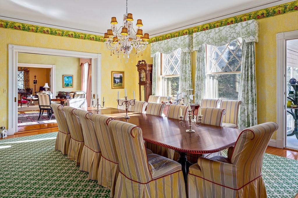 The formal dining room features a long wooden table, striped chairs, a crystal chandelier, and diamond-pane windows overlooking the property. | Source: Facebook/LegacySIR
