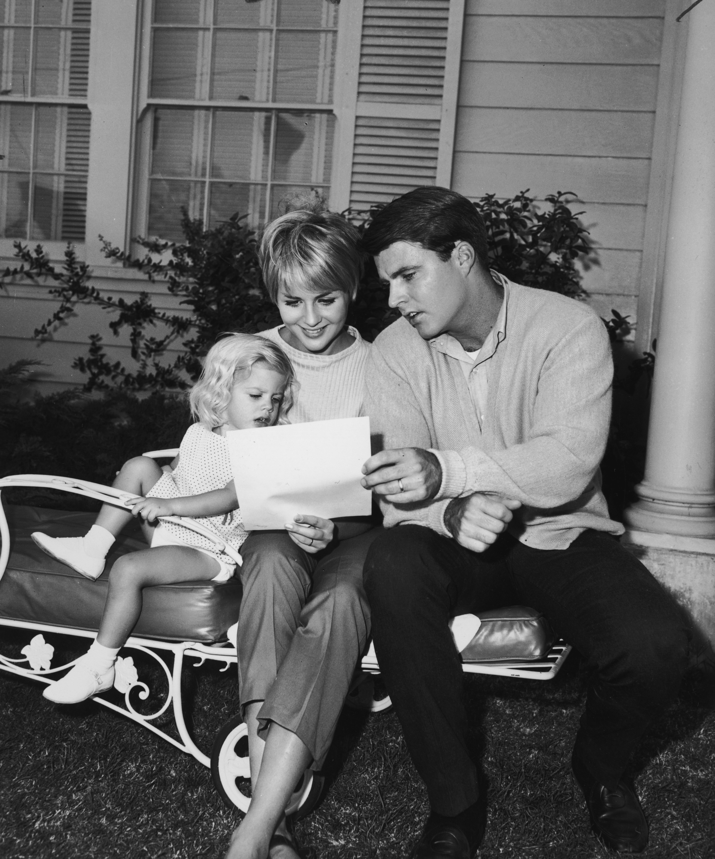 Rick Nelson (1940-1985) sits outdoors on a lawn chair with his wife Kristin Harmon and their daughter Tracy | Source: Getty Images