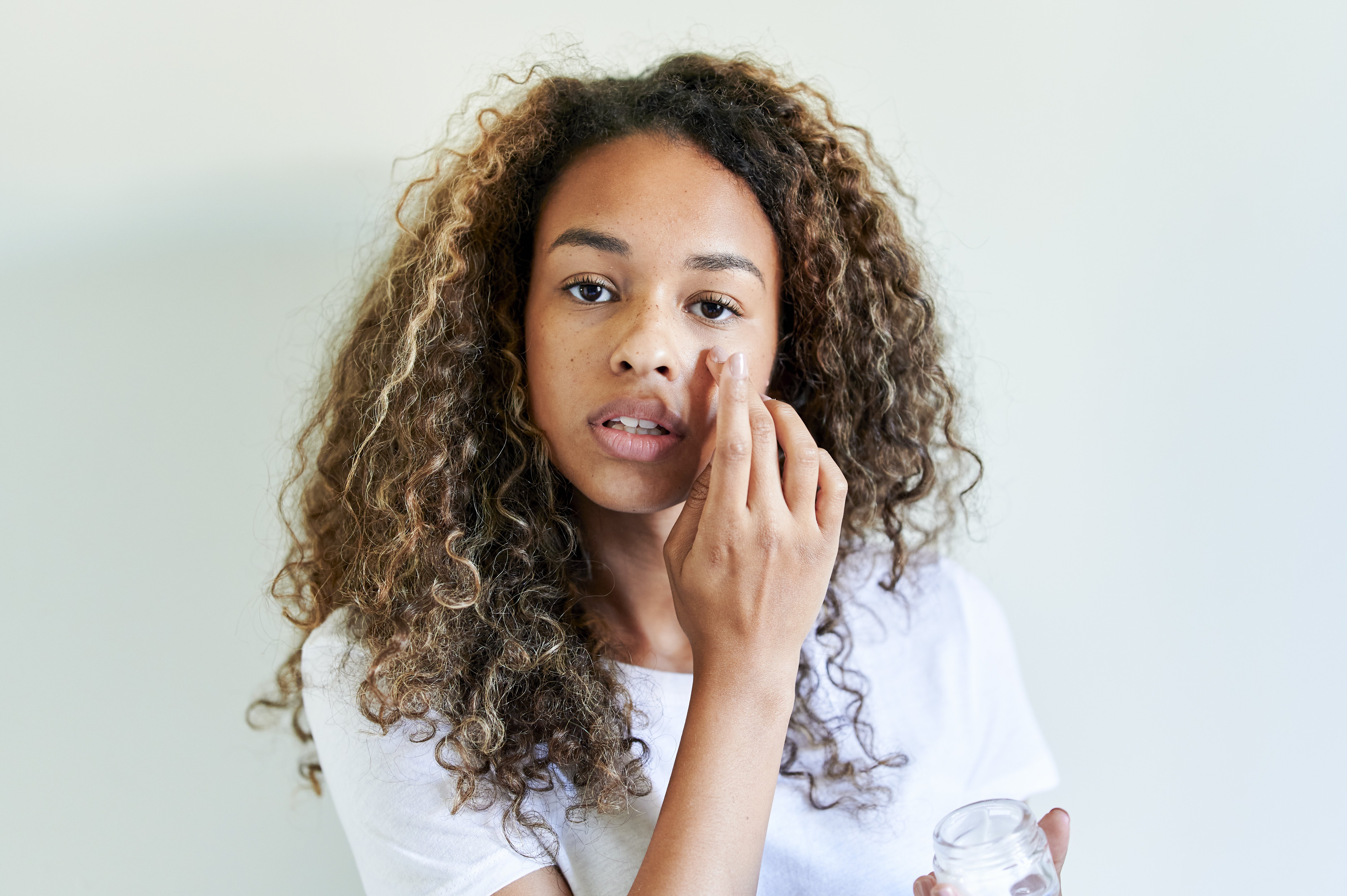 Young woman applying facial cream. | Source: Getty Images