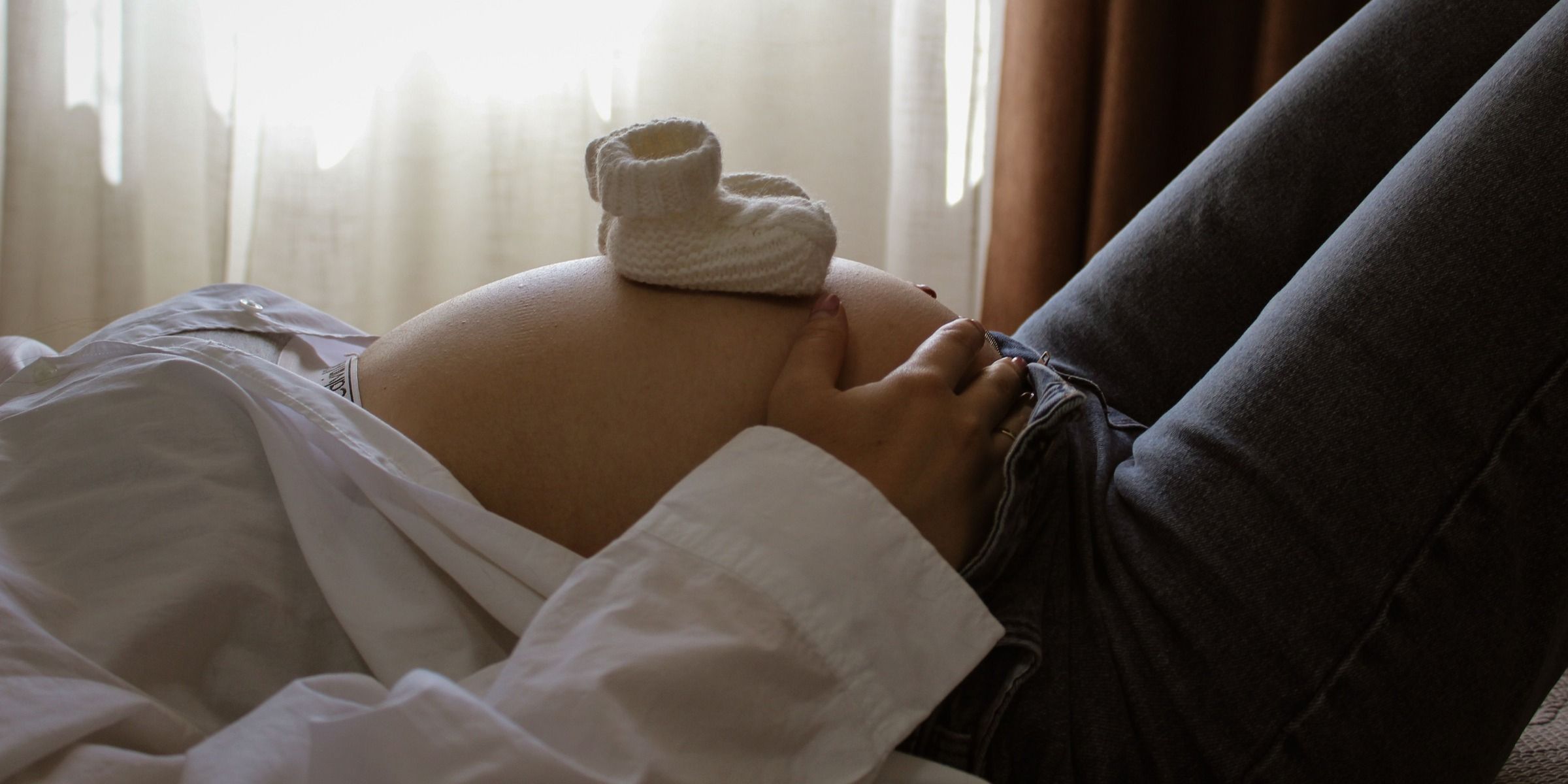 An expectant mother rests with baby booties on her stomach | Source: Pexels