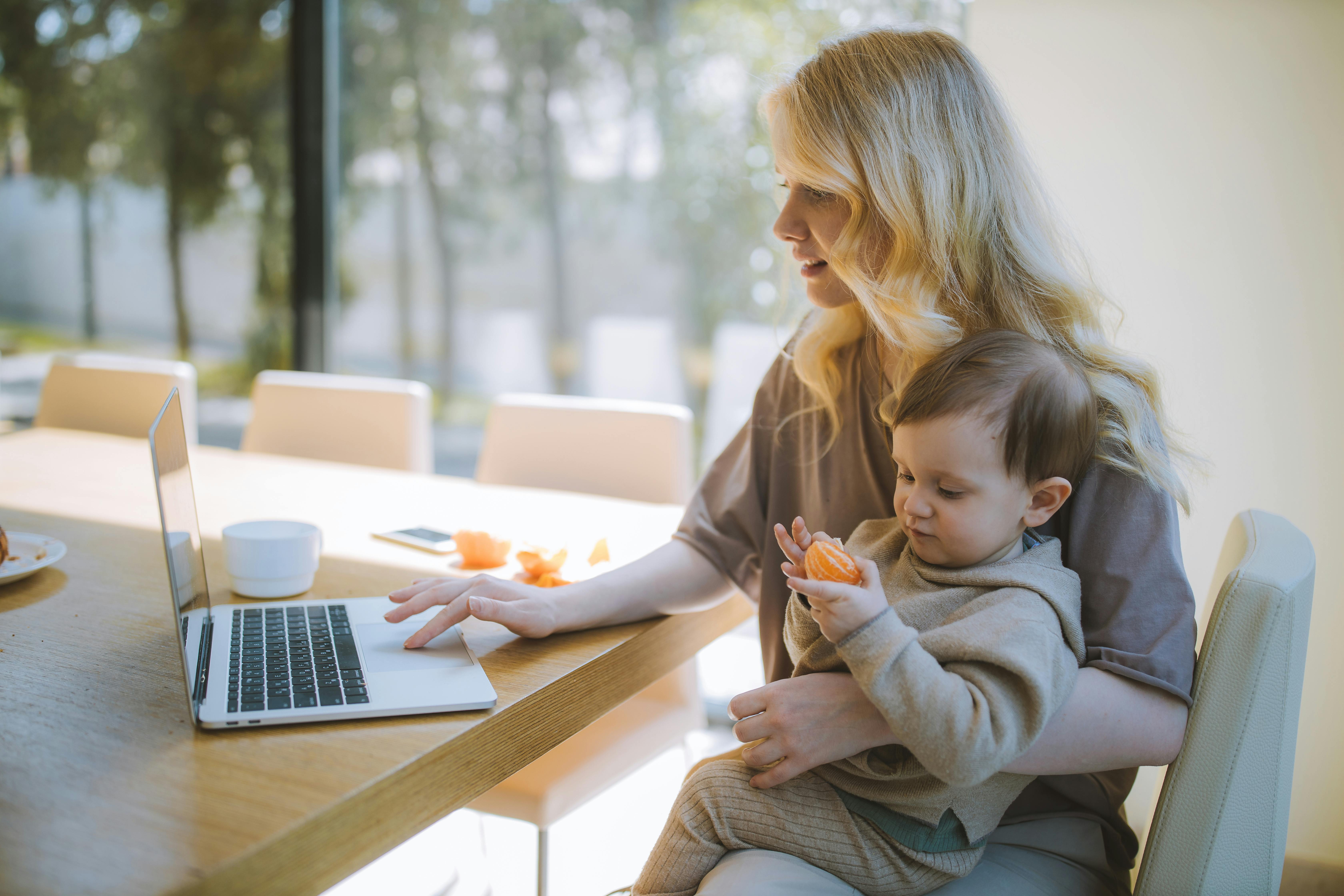 A woman carrying her baby as she does some work at home | Source: Pexels