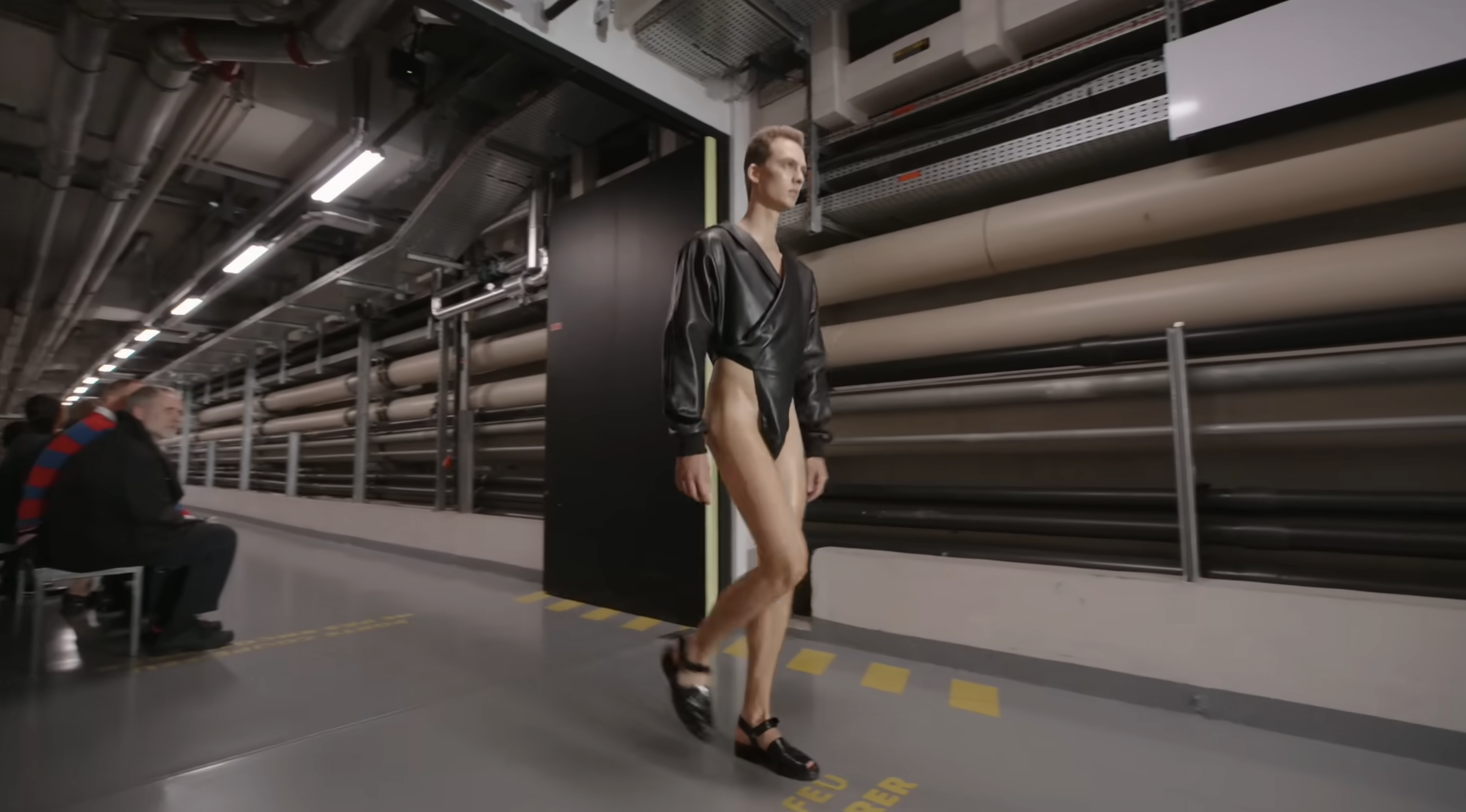 The model rounds the corner, revealing just how high the bodysuit’s cuts go. He pairs the look with black open shoes, adding to the futuristic vibe — a glimpse of what daring fashion might look like in the years ahead. From a post dated October 5, 2025. Source: Youtube/@jeanpaulgaultier