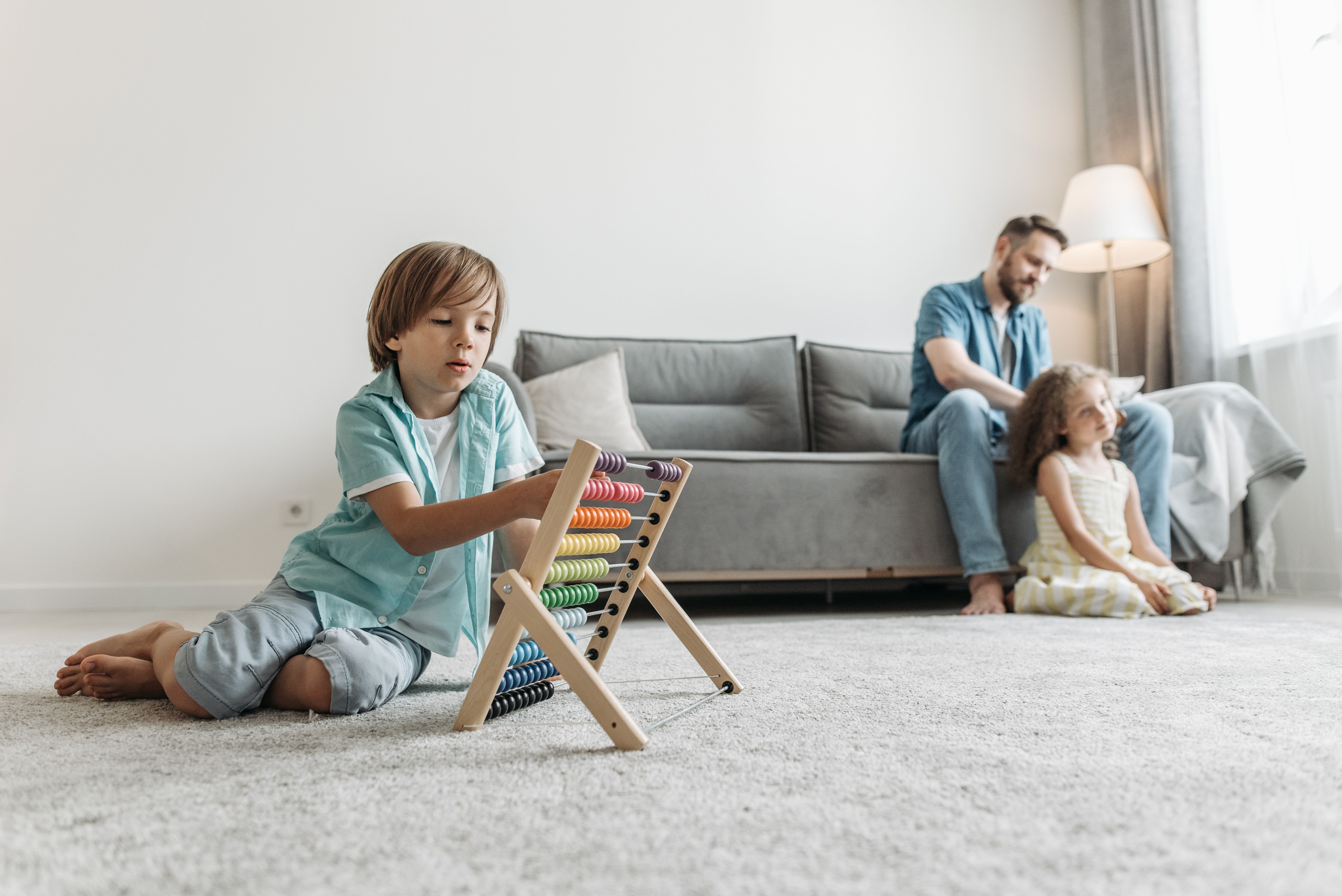 A father combing his daughter's hair while the son plays with an abacus alone | Source: Pexels
