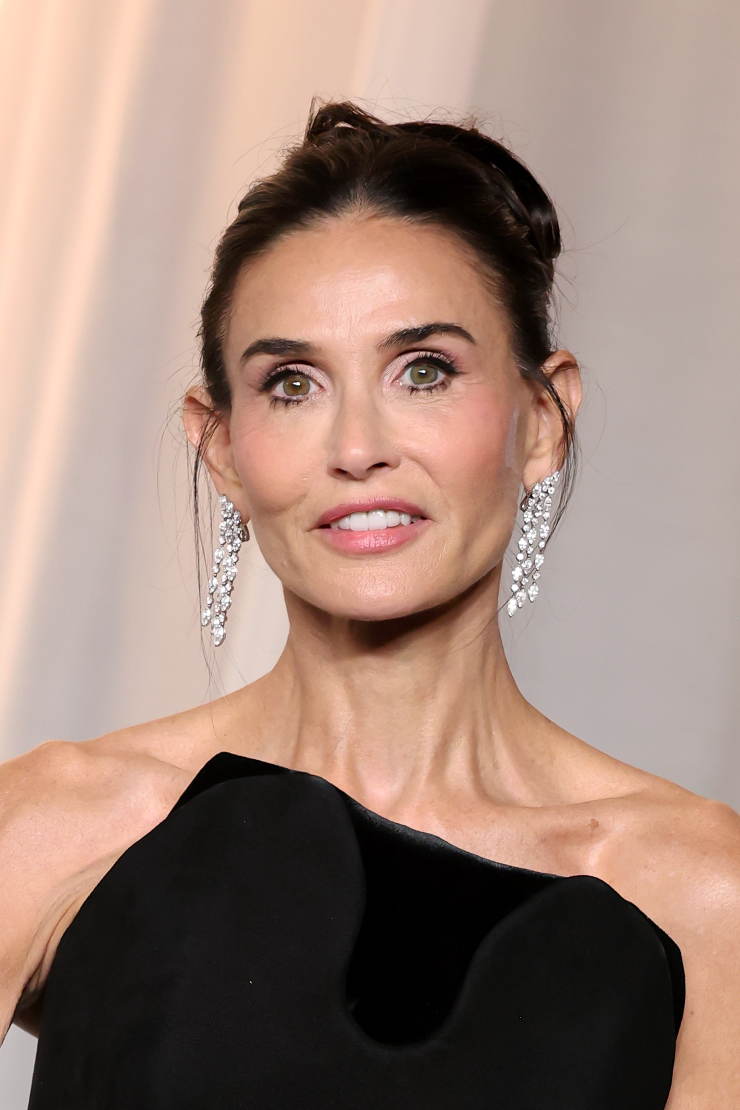 In a close-up portrait, Moore pairs her sleek updo and soft pink makeup with cascading diamond earrings and the sculptural neckline of her black bodice.