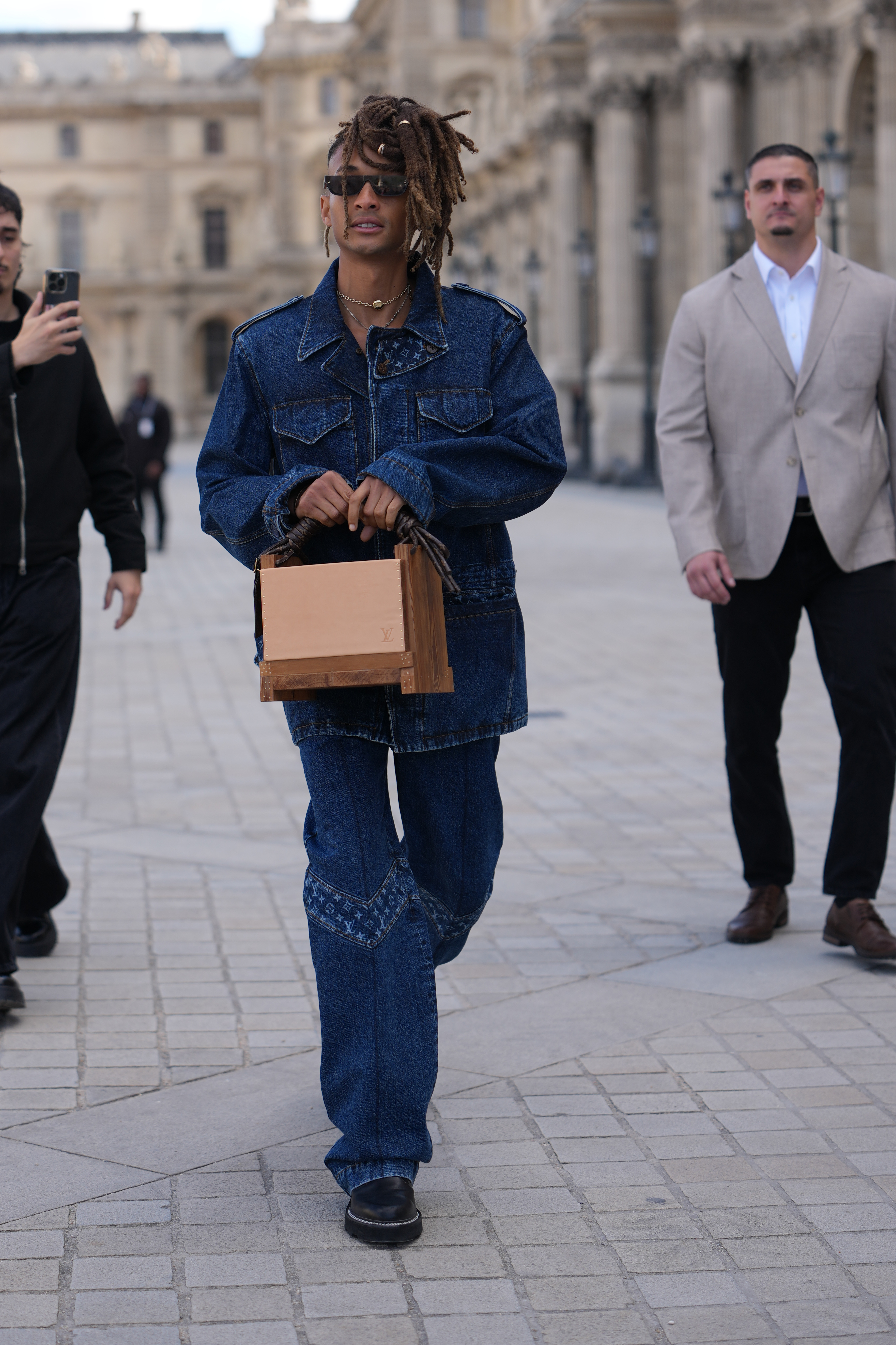 Jaden Smith was spotted outside Louis Vuitton during Paris Fashion Week Women’s Spring/Summer 2026 in France. He donned a dark indigo denim jacket, paired with matching relaxed straight-leg jeans. He completed the look with a wooden box clutch and black leather platform slip-on shoes with a low block heel.