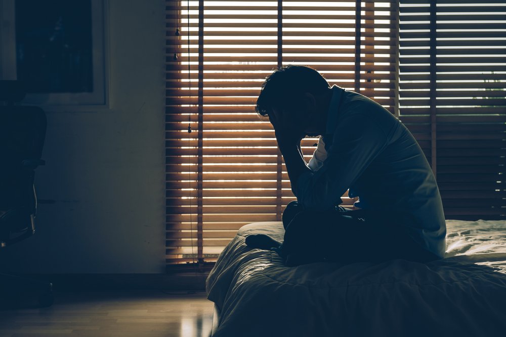 An unhappy and stressed out businessman sitting with his head in hands on the bed in a dark bedroom | Photo: Shutterstock/TZIDO SUN