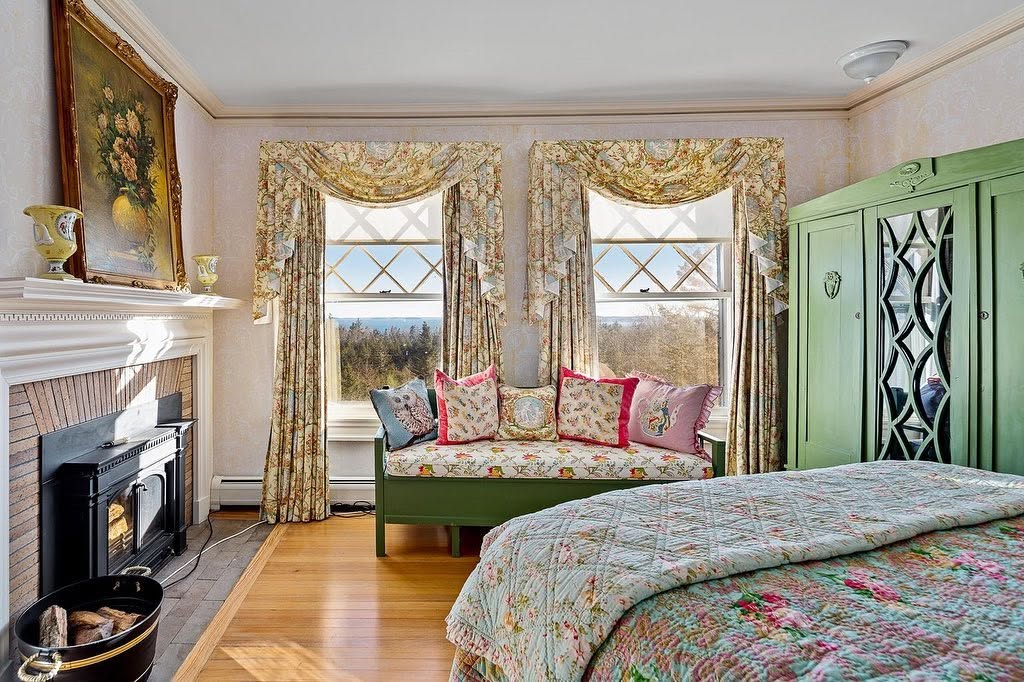 Another bedroom includes a fireplace, floral textiles, a window-side bench, and a pale green wardrobe with decorative mirrored doors. | Source: Facebook/LegacySIR