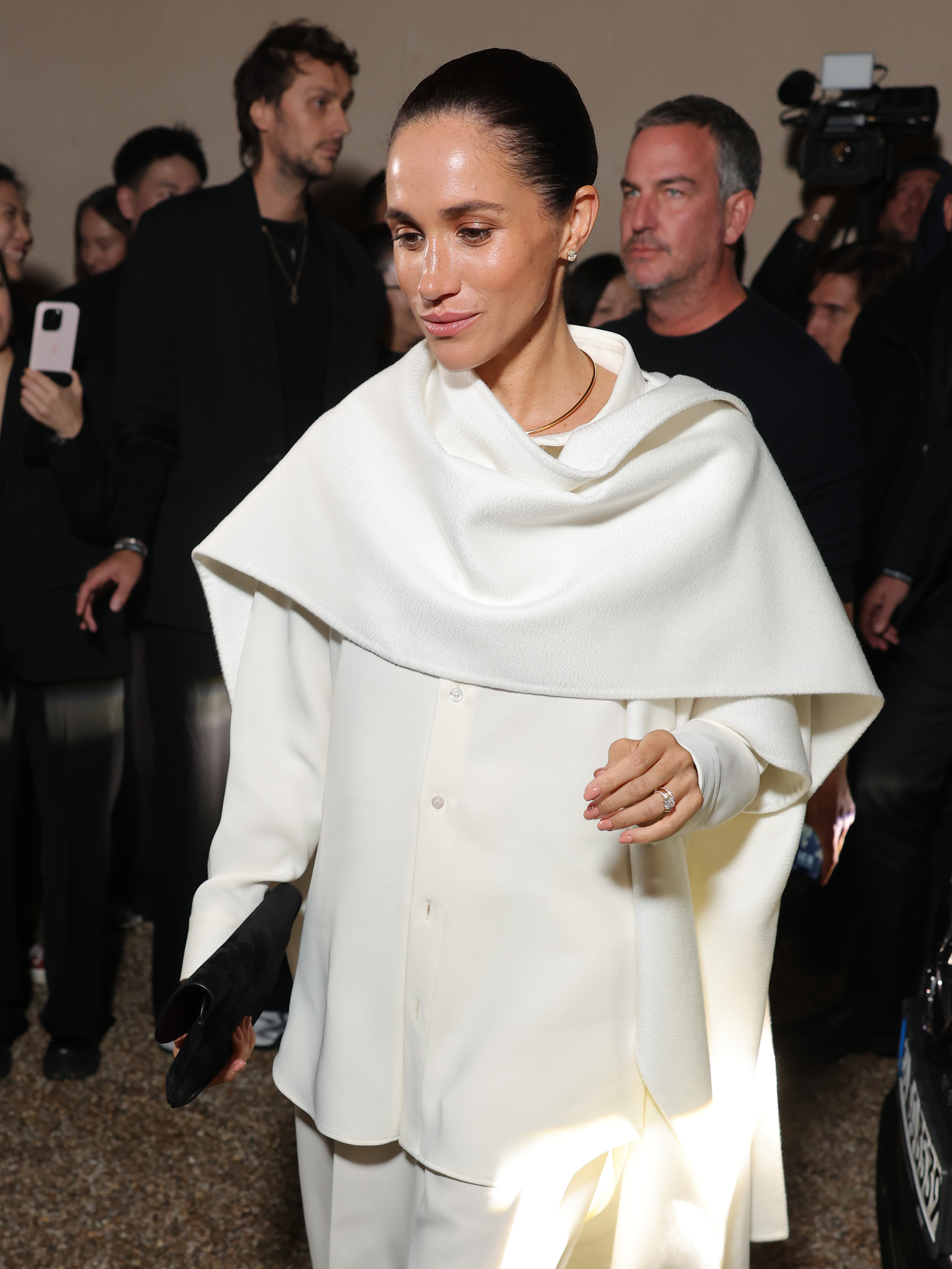 Meghan Markle, Duchess of Sussex, completed her look with a cascading white cape, pointed-toe black pumps, and a sleek clutch. Her hair was pulled into a sleek bun, showcasing her glowing, impeccably done makeup.