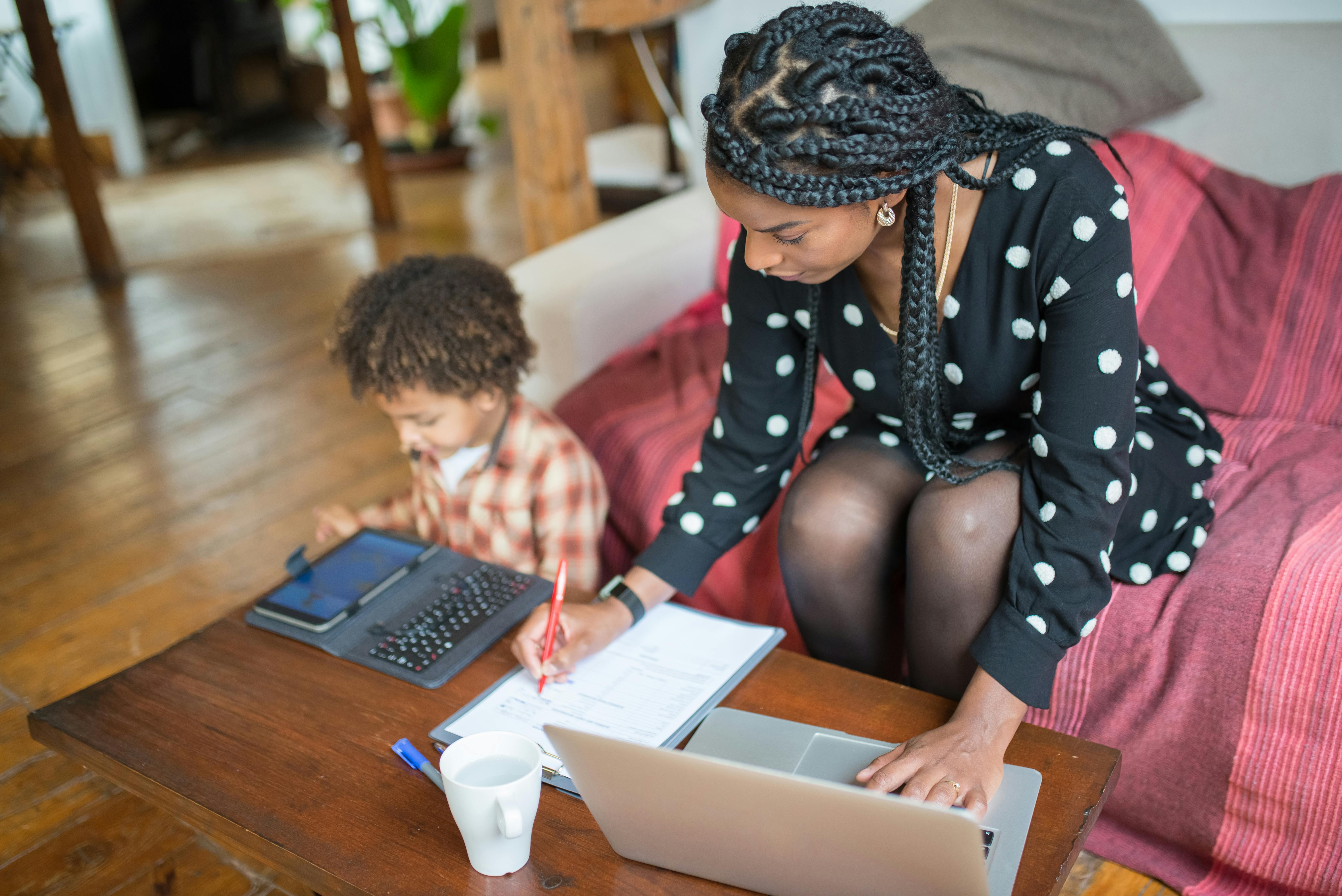 Mother working at home with her child seated next to her | Source: Pexels