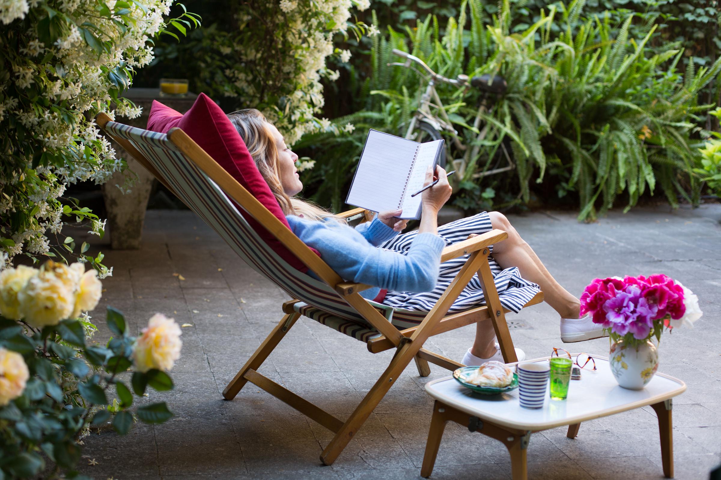 A woman relaxing on a deck chair while journaling | Source: Getty Images