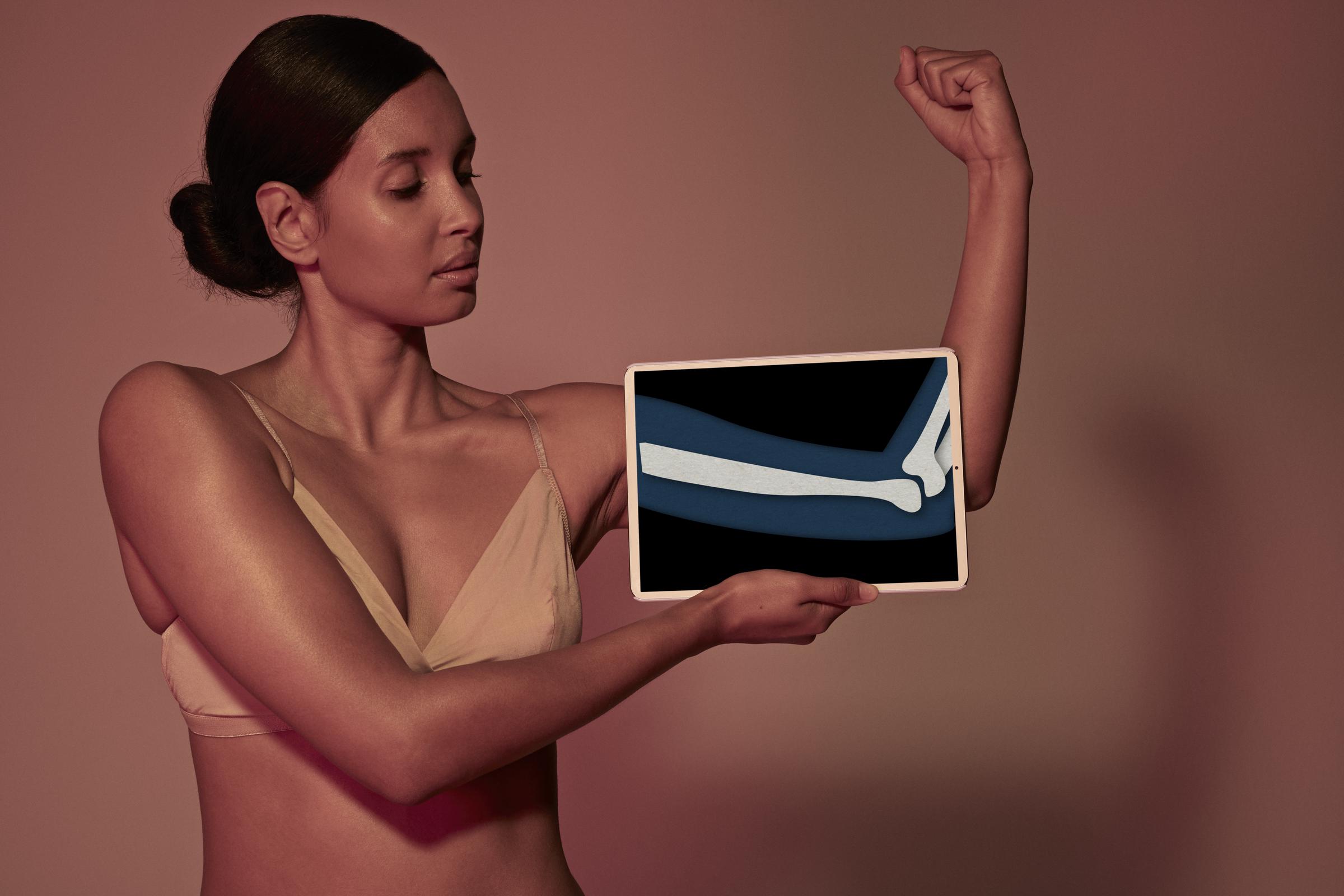 A woman holding a tablet in front of her arm to display a coloured x-ray illustration | Source: Getty Images